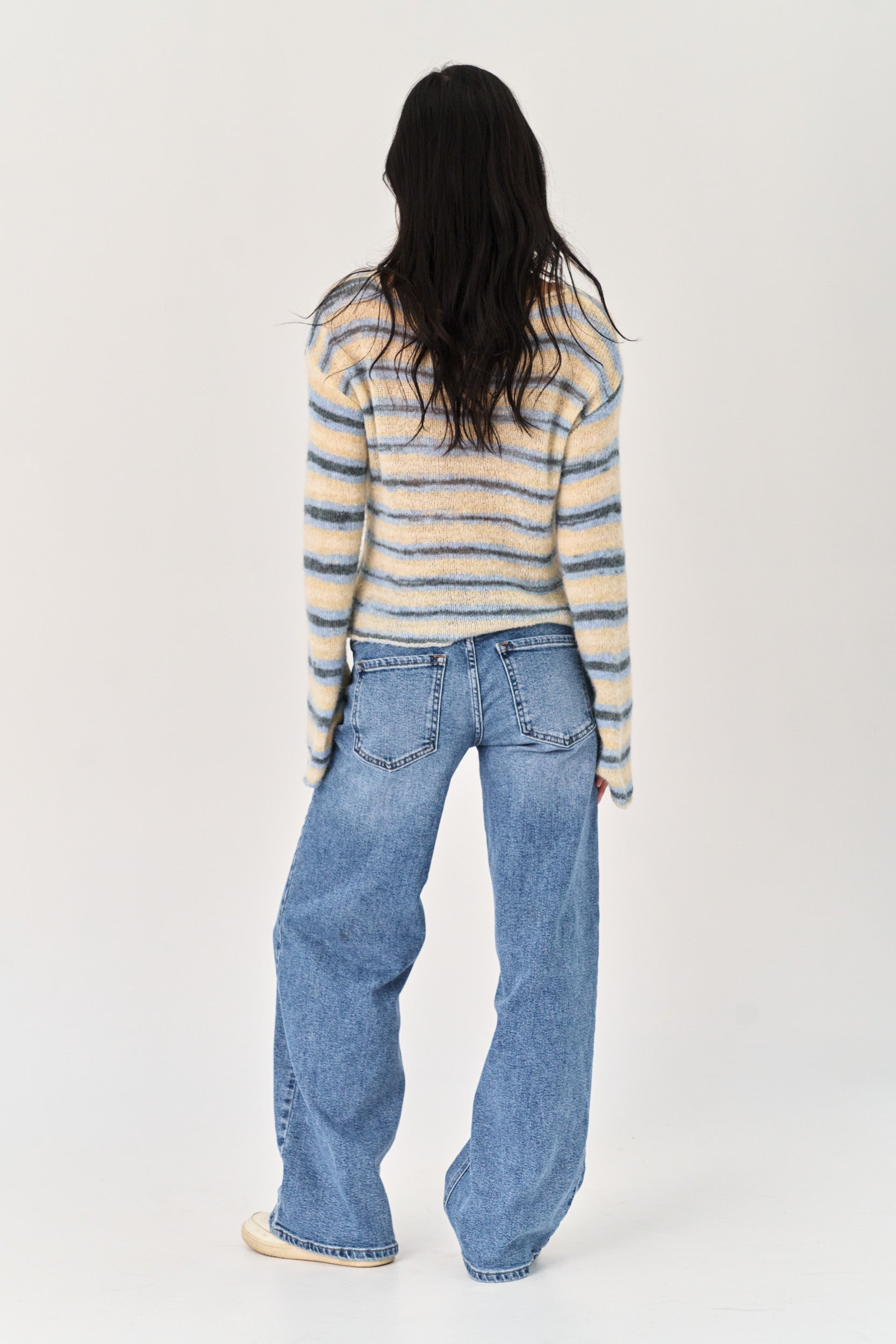 Person wearing a striped sweater and blue jeans on a white background