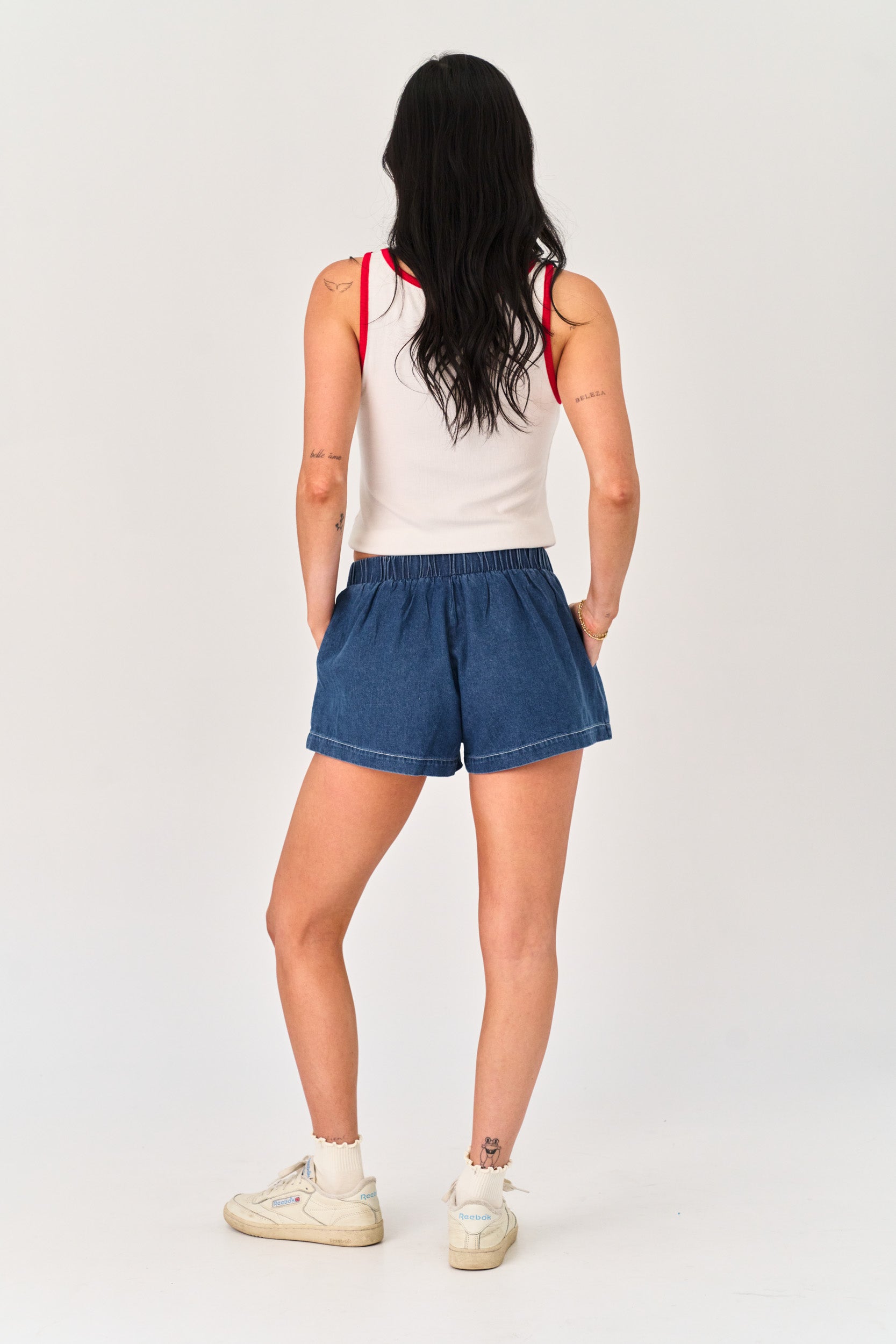 Person wearing a white tank top and blue denim shorts on a plain background