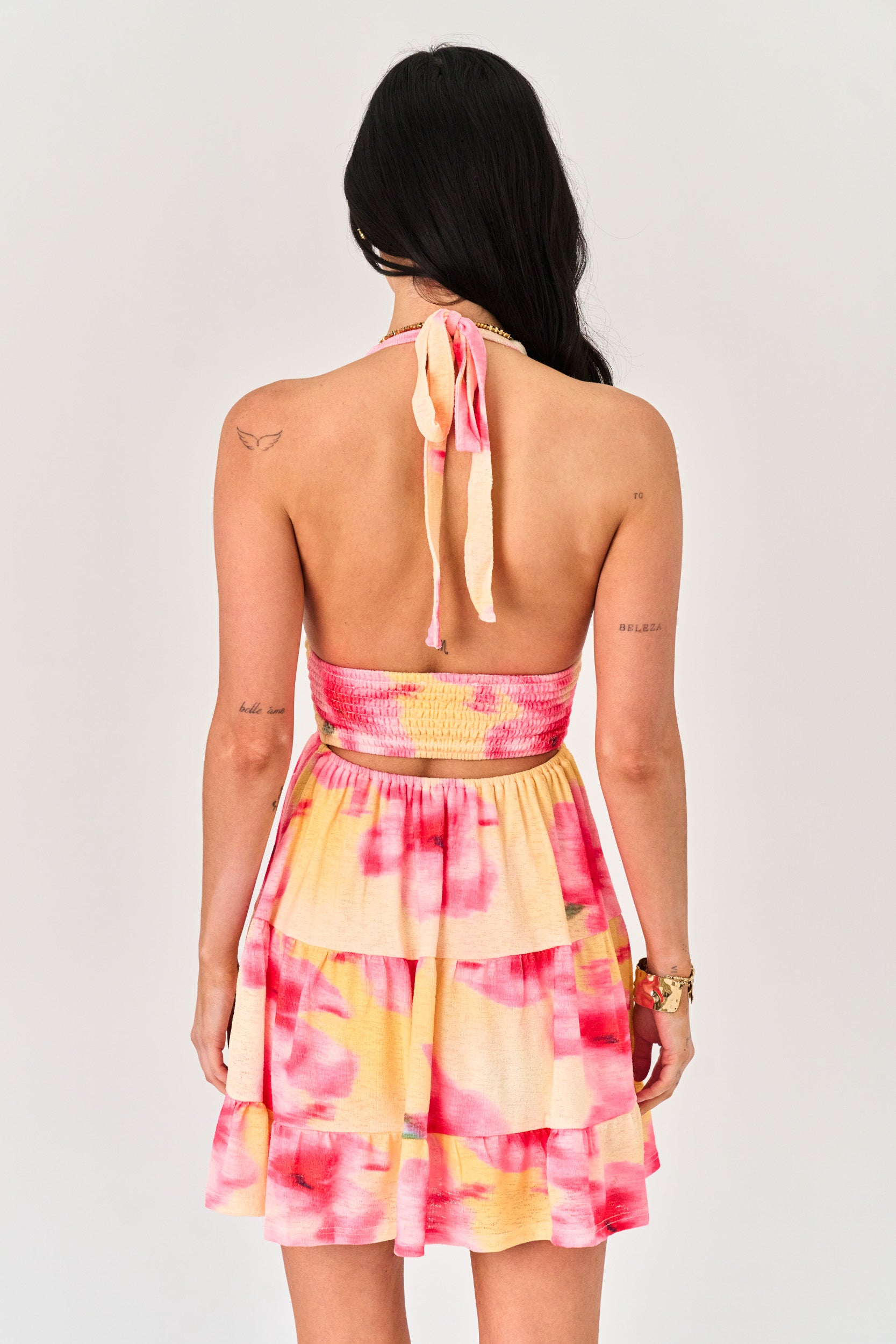 Woman wearing a pink and yellow tie-dye dress with a plain background