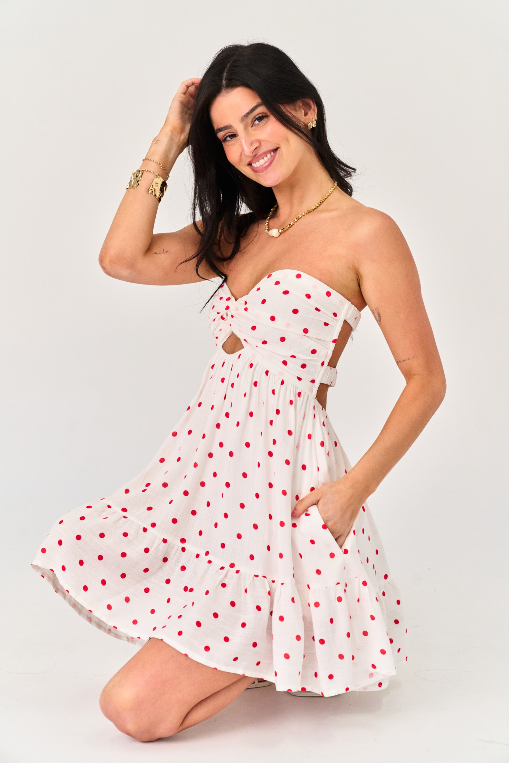 Woman wearing a white dress with red polka dots on a plain background