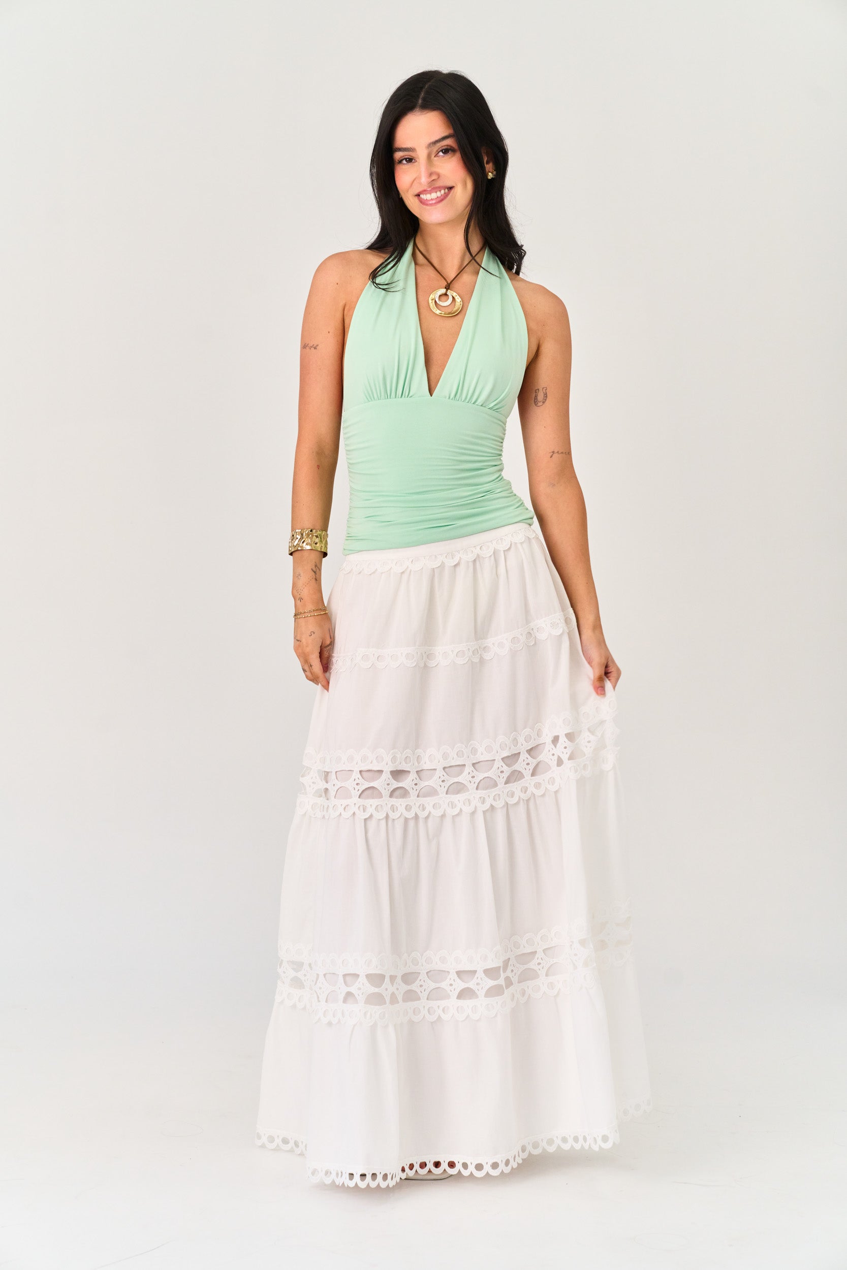 Woman wearing a green halter top and white lace-trimmed skirt on a white background