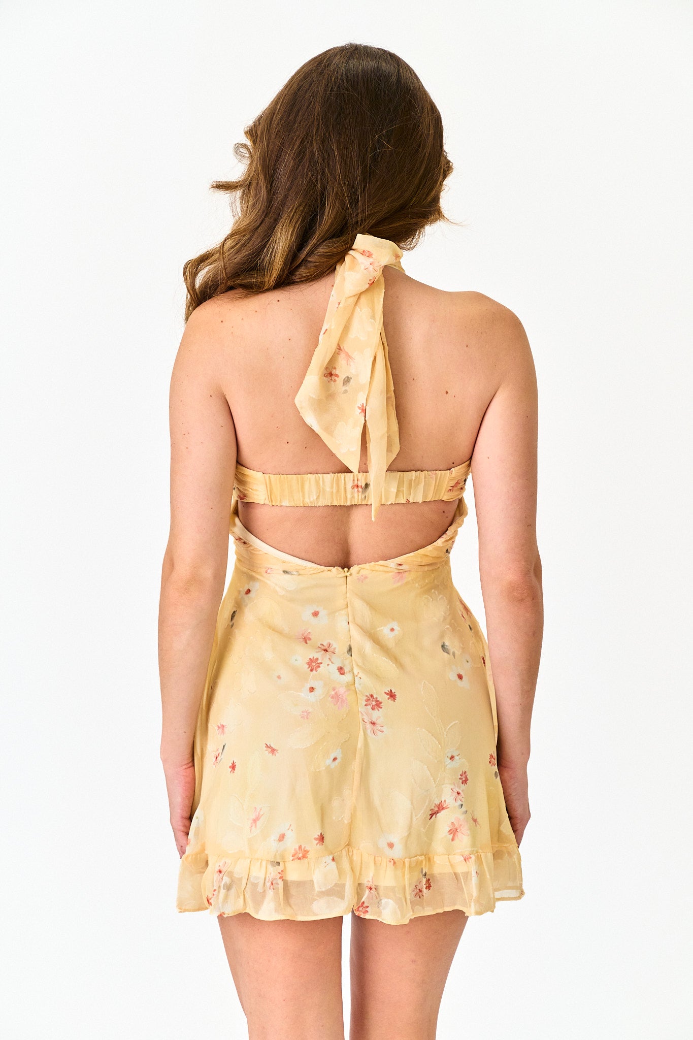 Woman wearing a yellow floral dress with a halter neck design on a white background
