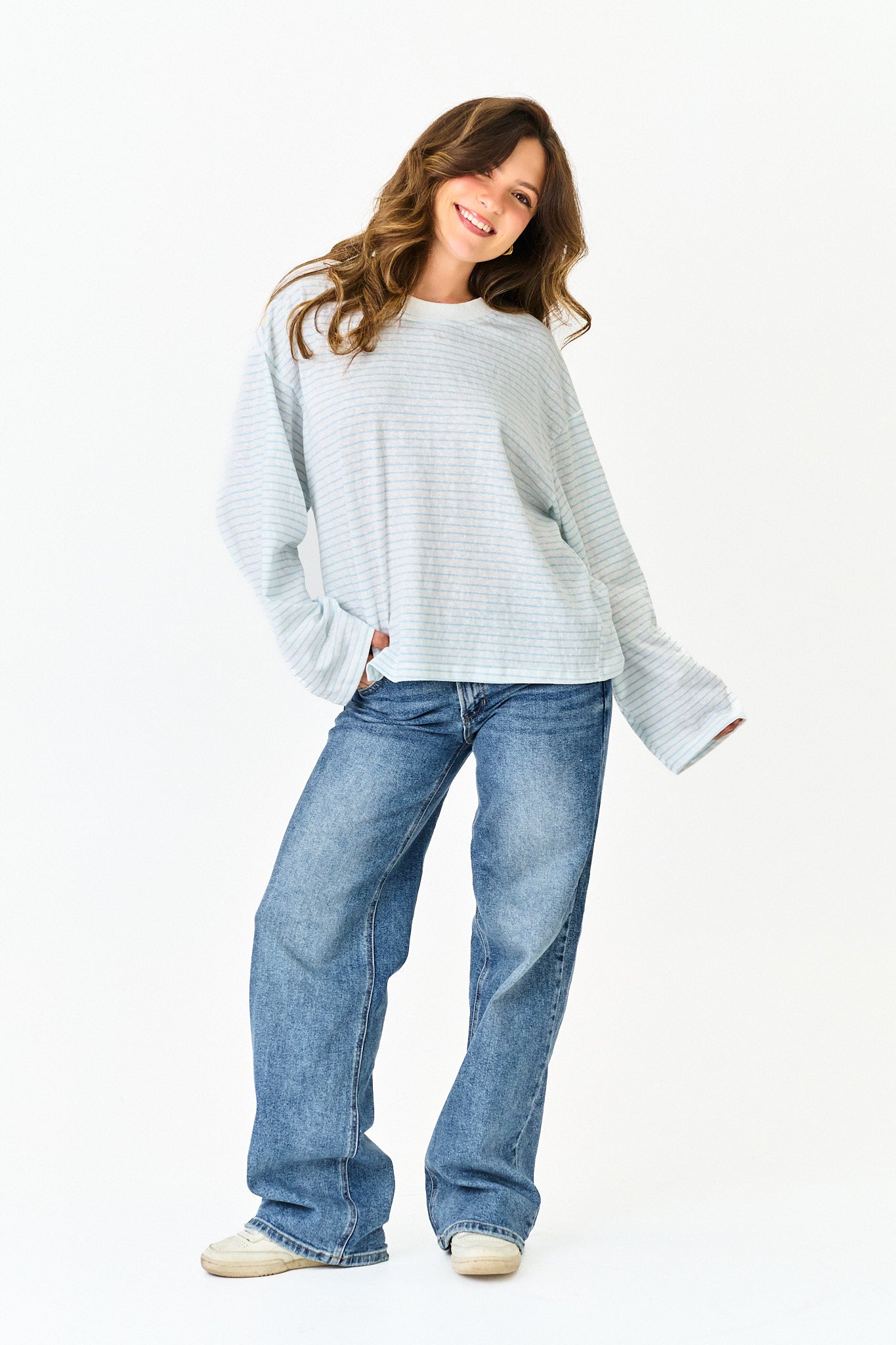Woman wearing a light gray sweater and blue jeans on a white background