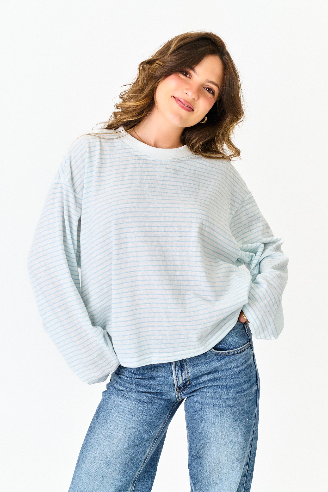 Woman wearing a light blue striped sweater and jeans on a white background