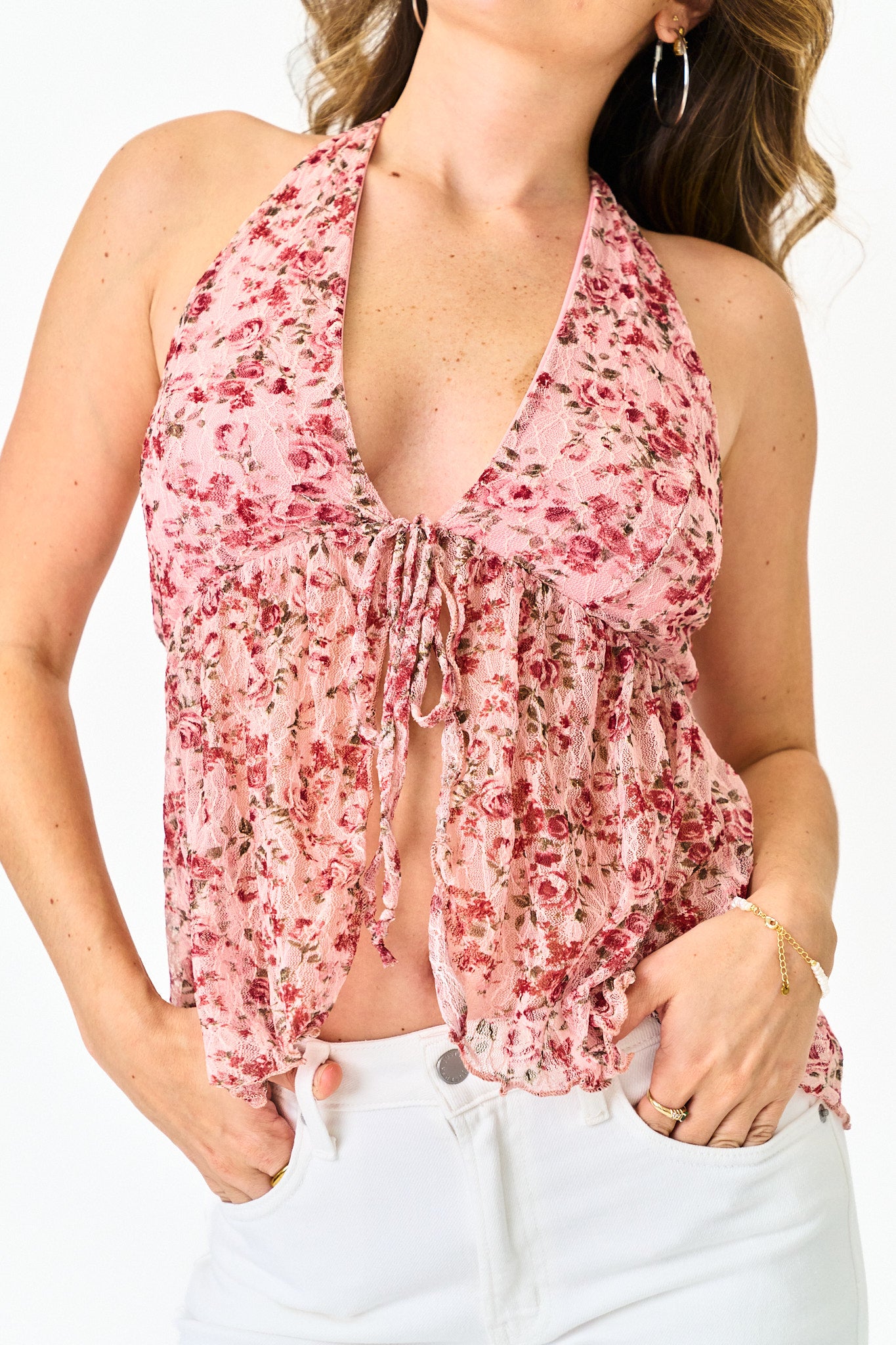 Woman wearing a pink floral halter top with white pants on a white background