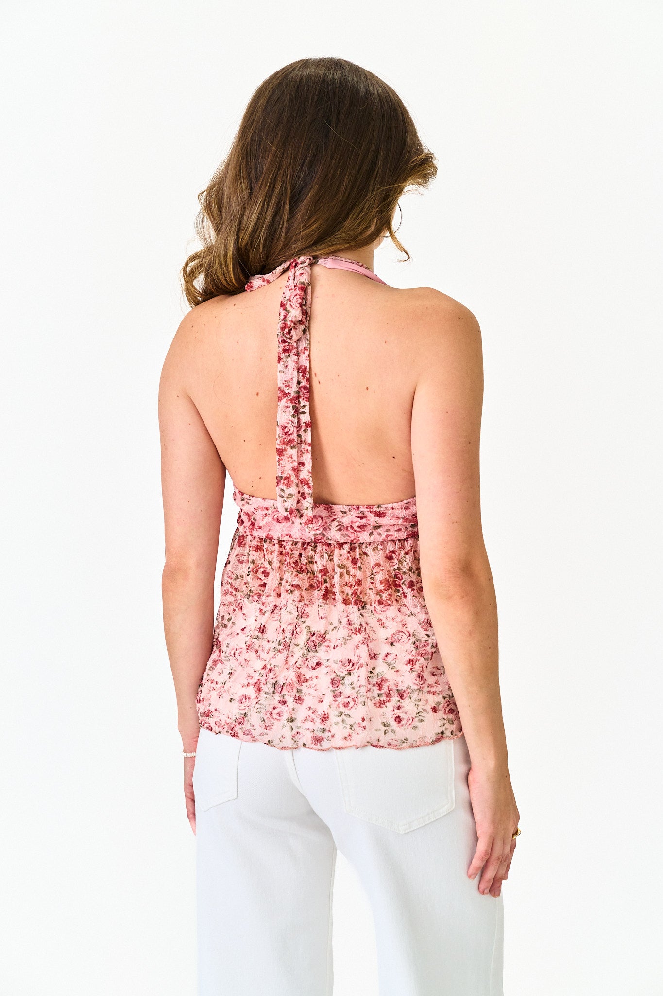 Woman wearing a floral halter top and white pants on a white background