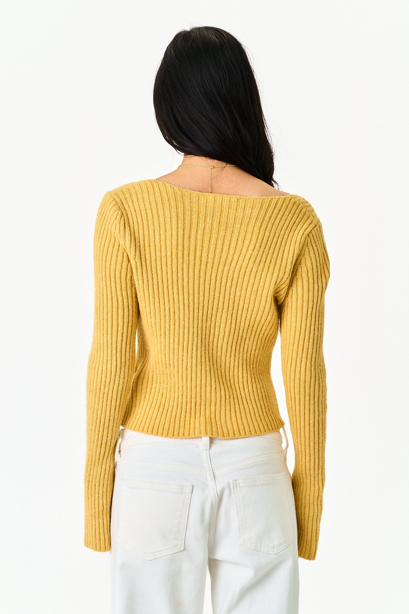 A woman shown from the back wearing a mustard yellow ribbed knit sweater with an off-the-shoulder neckline and white pants, against a plain white background.