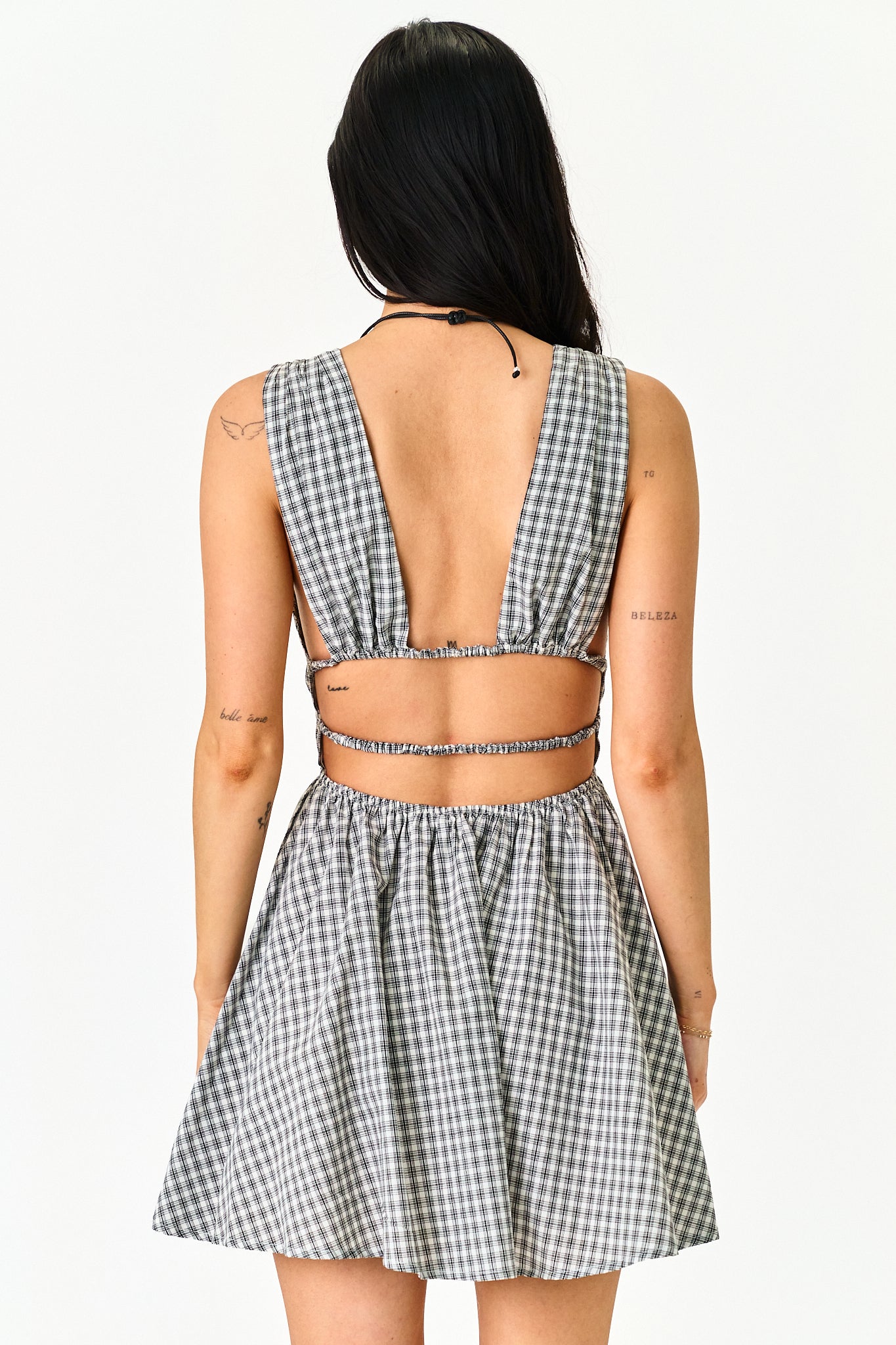 A woman shown from the back wearing a sleeveless black and white gingham check mini dress with a cutout back and matching flared skirt, against a plain light background.