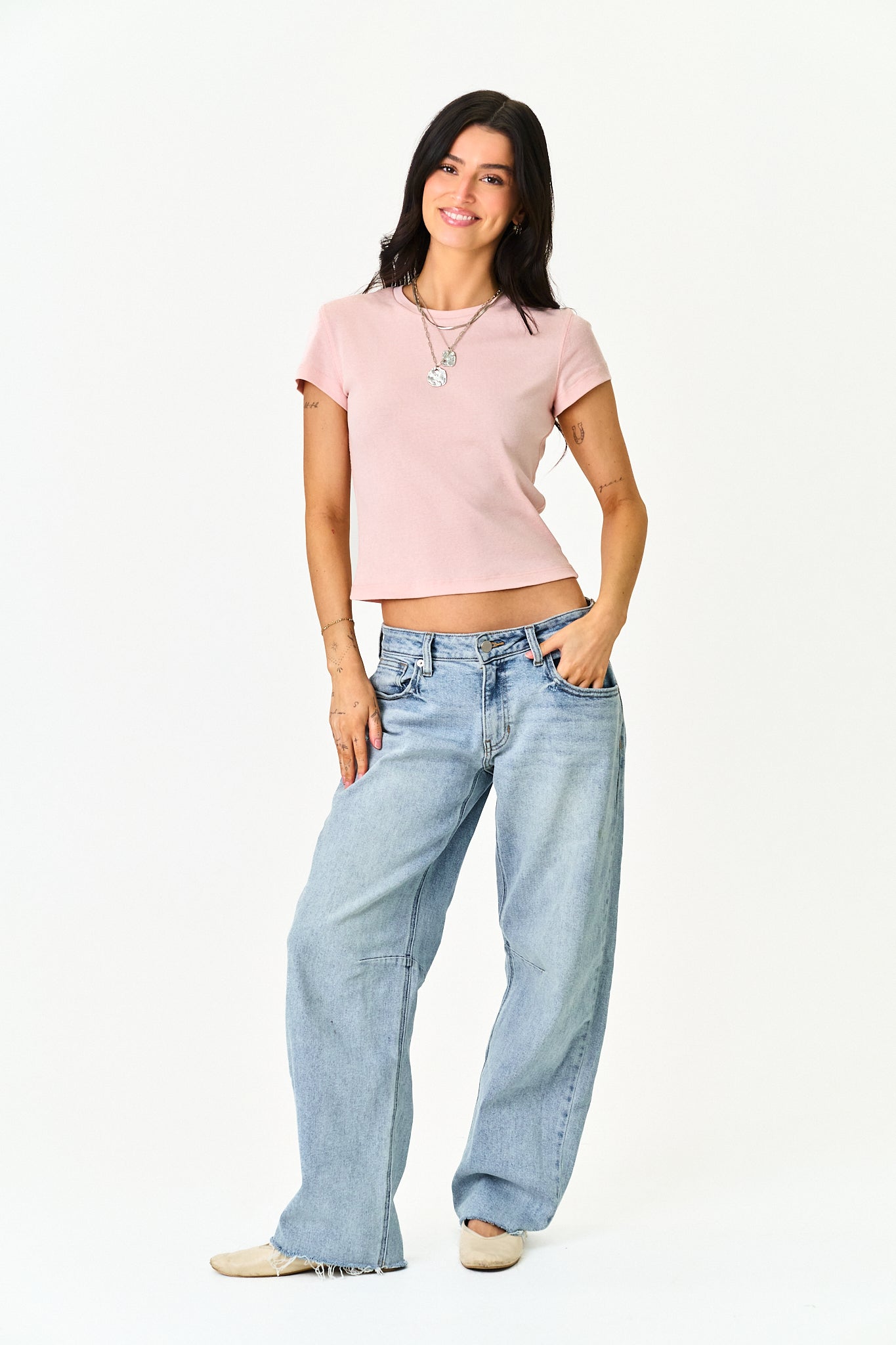 A woman modeling a light pink short-sleeve crop top and wide-leg light blue jeans against a plain white studio background.