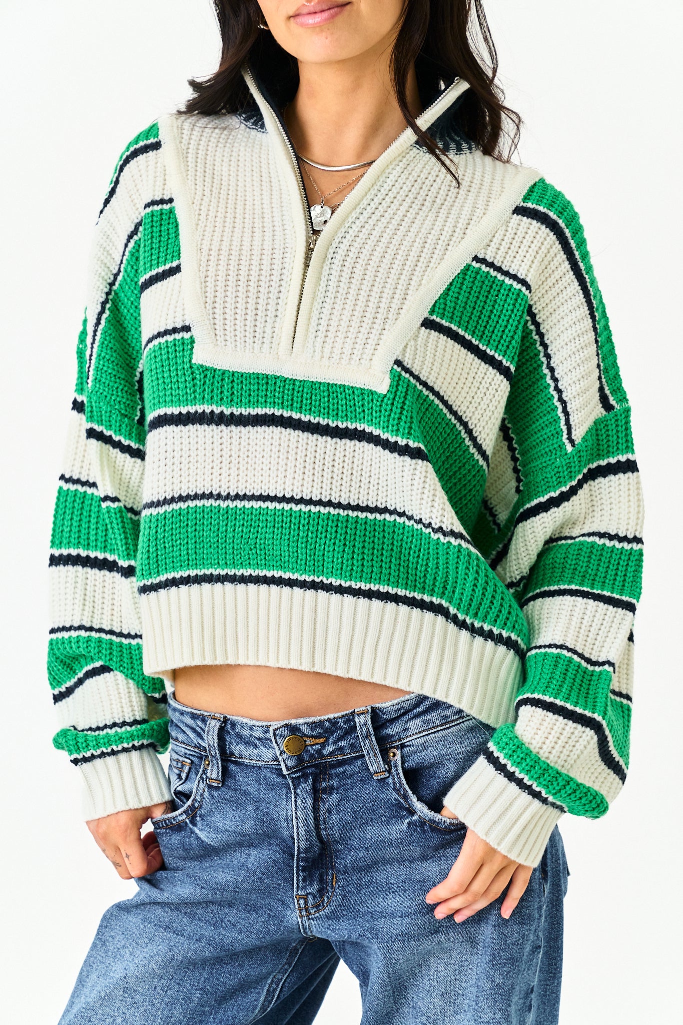 A woman wearing a cropped, long-sleeve knit half-zip sweater with horizontal stripes in green, cream, and black, paired with blue jeans.