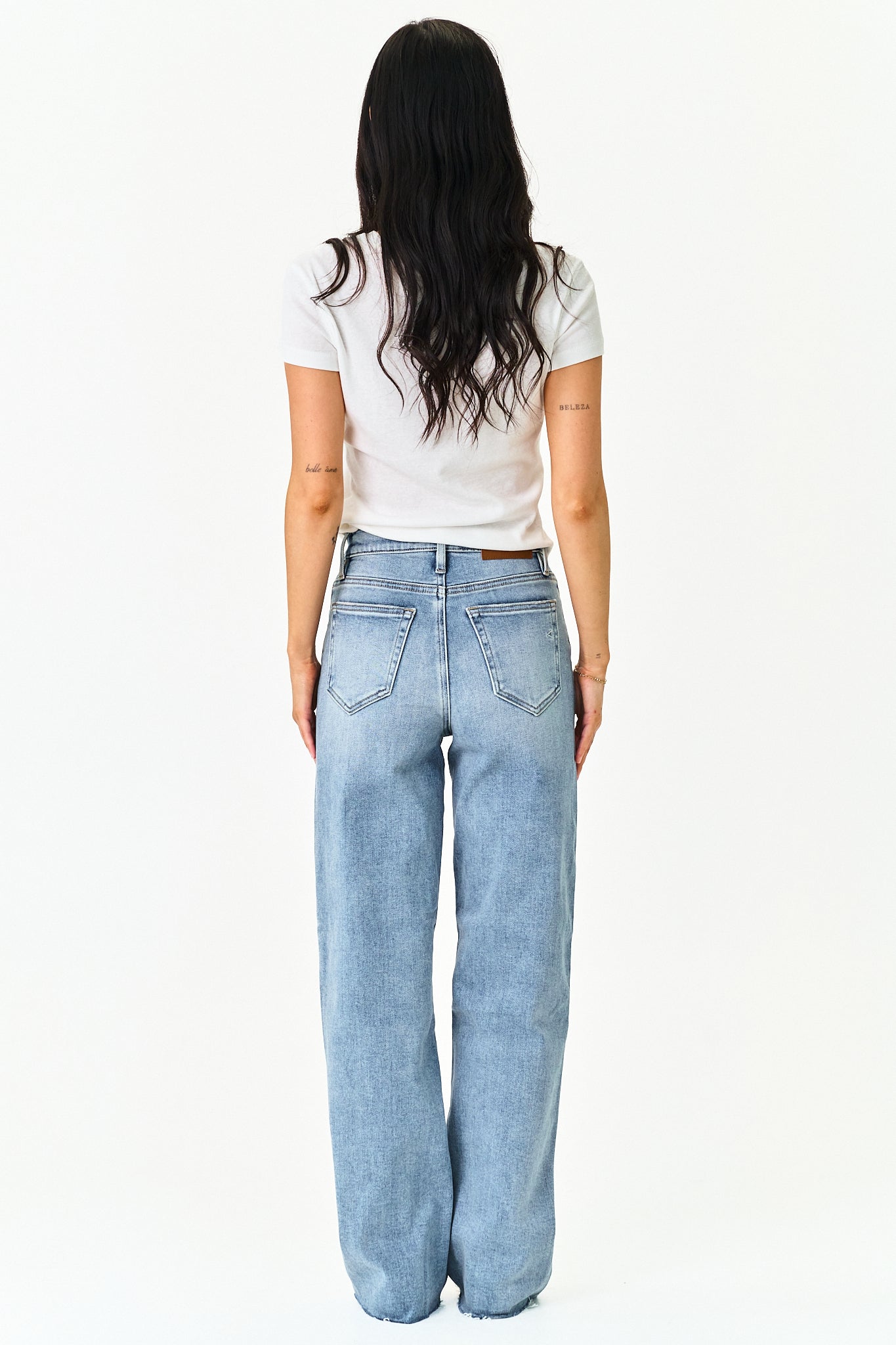 A woman viewed from behind wearing a white short-sleeve t-shirt and light-wash wide-leg denim jeans against a plain white background.