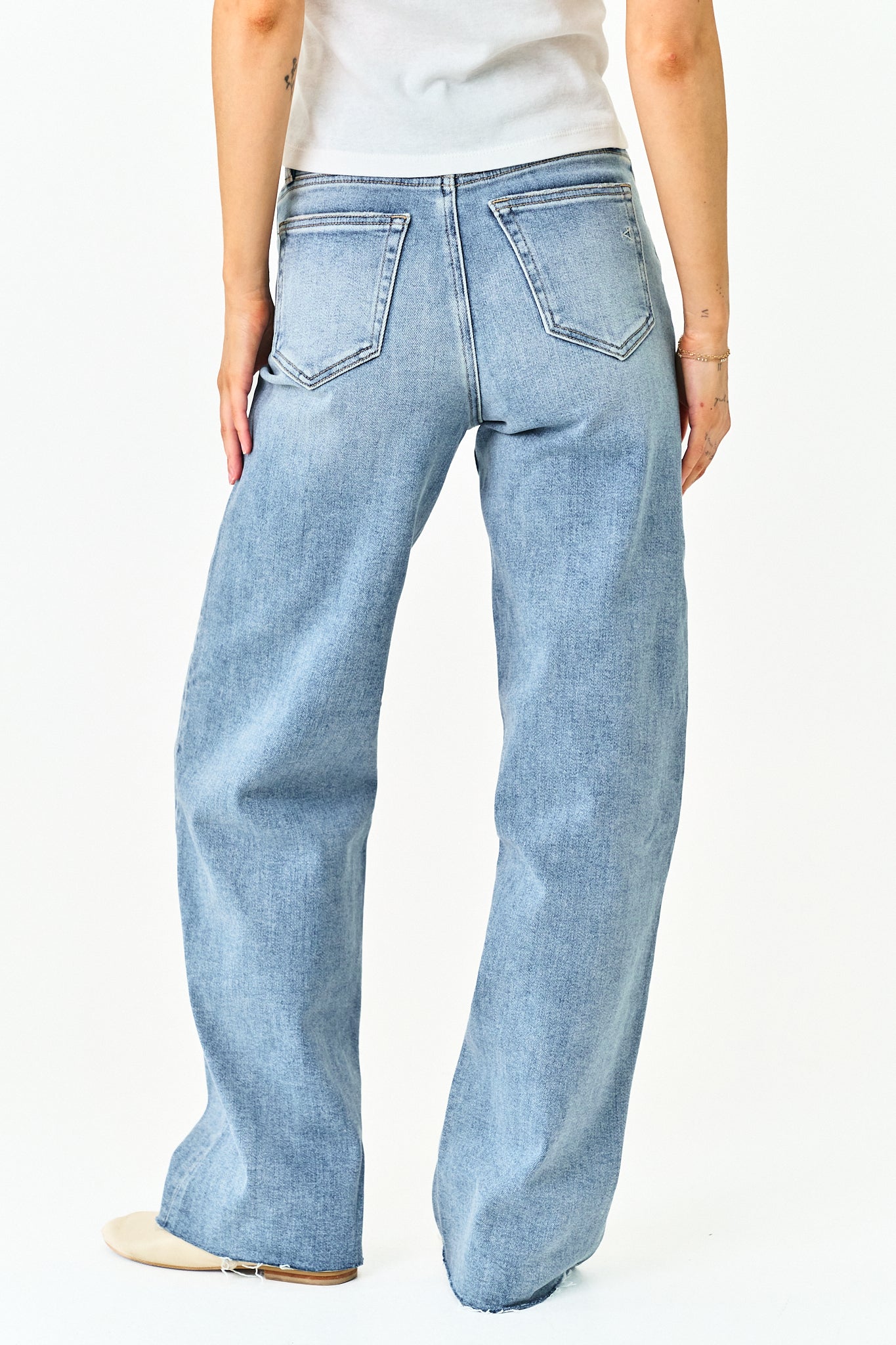 A person shown from the back wearing light-wash wide-leg jeans, a white top, and beige shoes against a plain white studio background.