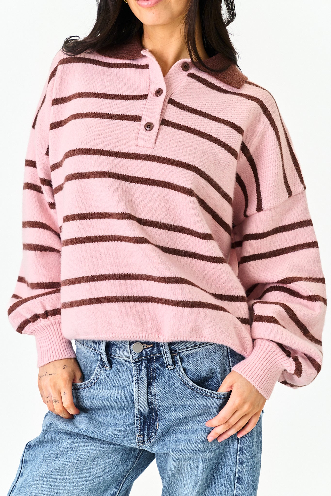 A woman wearing a pink and dark brown striped knit polo sweater with blue jeans, shown from the waist up against a plain white background.