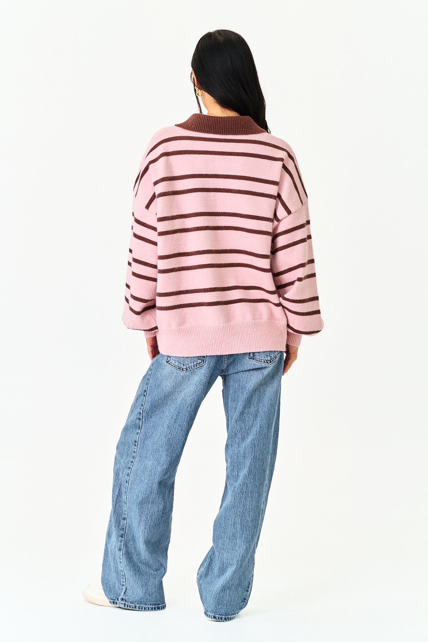 A model shown from the back wearing a pink and dark brown striped knit sweater and wide-leg blue jeans against a plain white background.