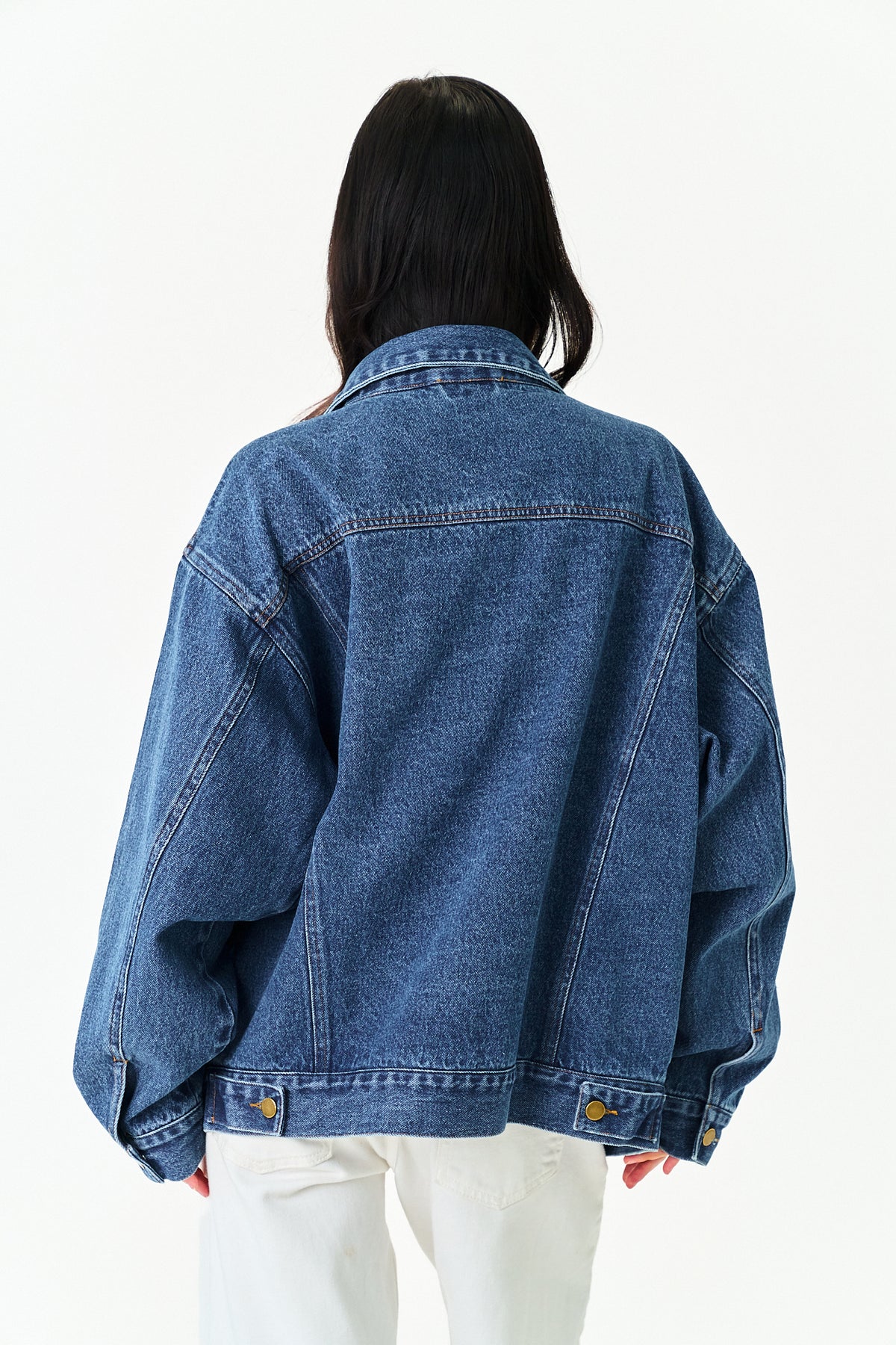 A person viewed from the back wearing an oversized blue denim jacket with white pants, photographed against a plain white studio background.