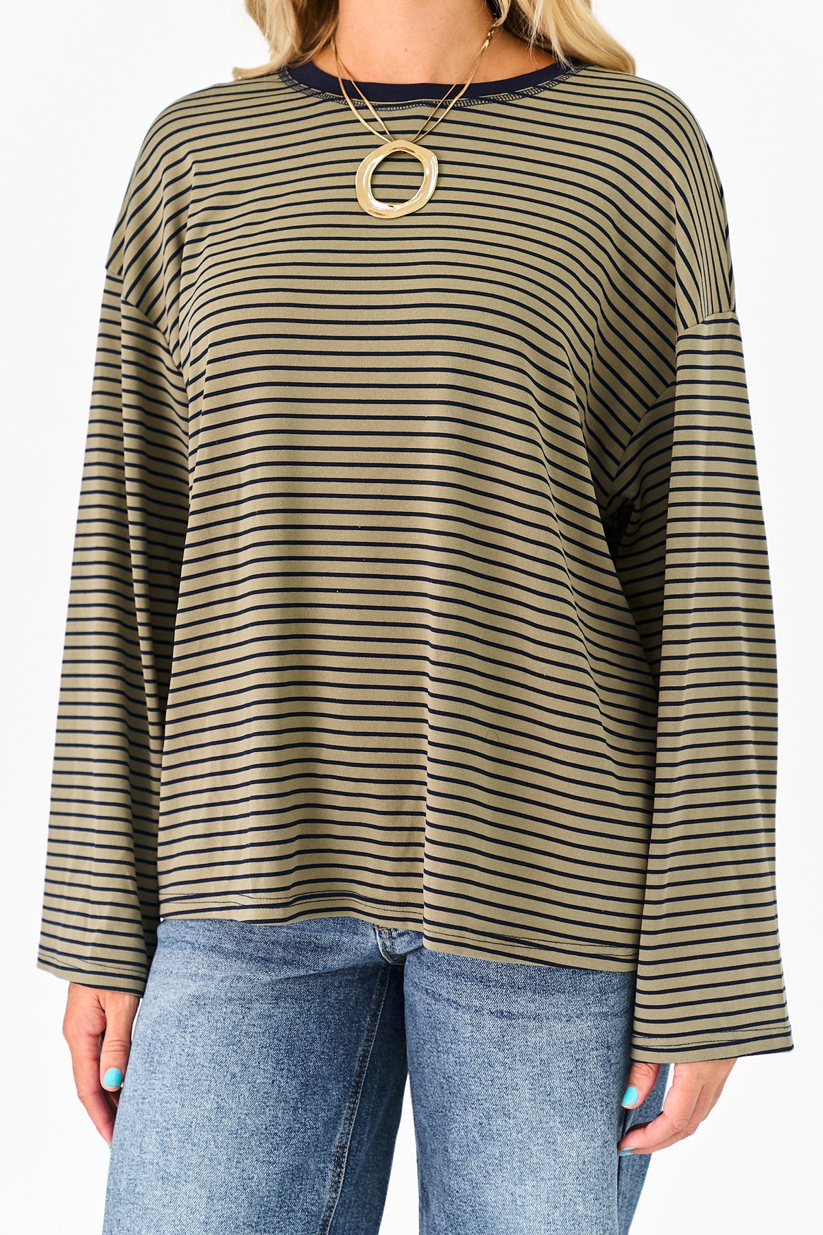A woman wearing a long-sleeve olive green and black striped top with blue jeans and a gold ring necklace, shown from the neck down against a plain white background.