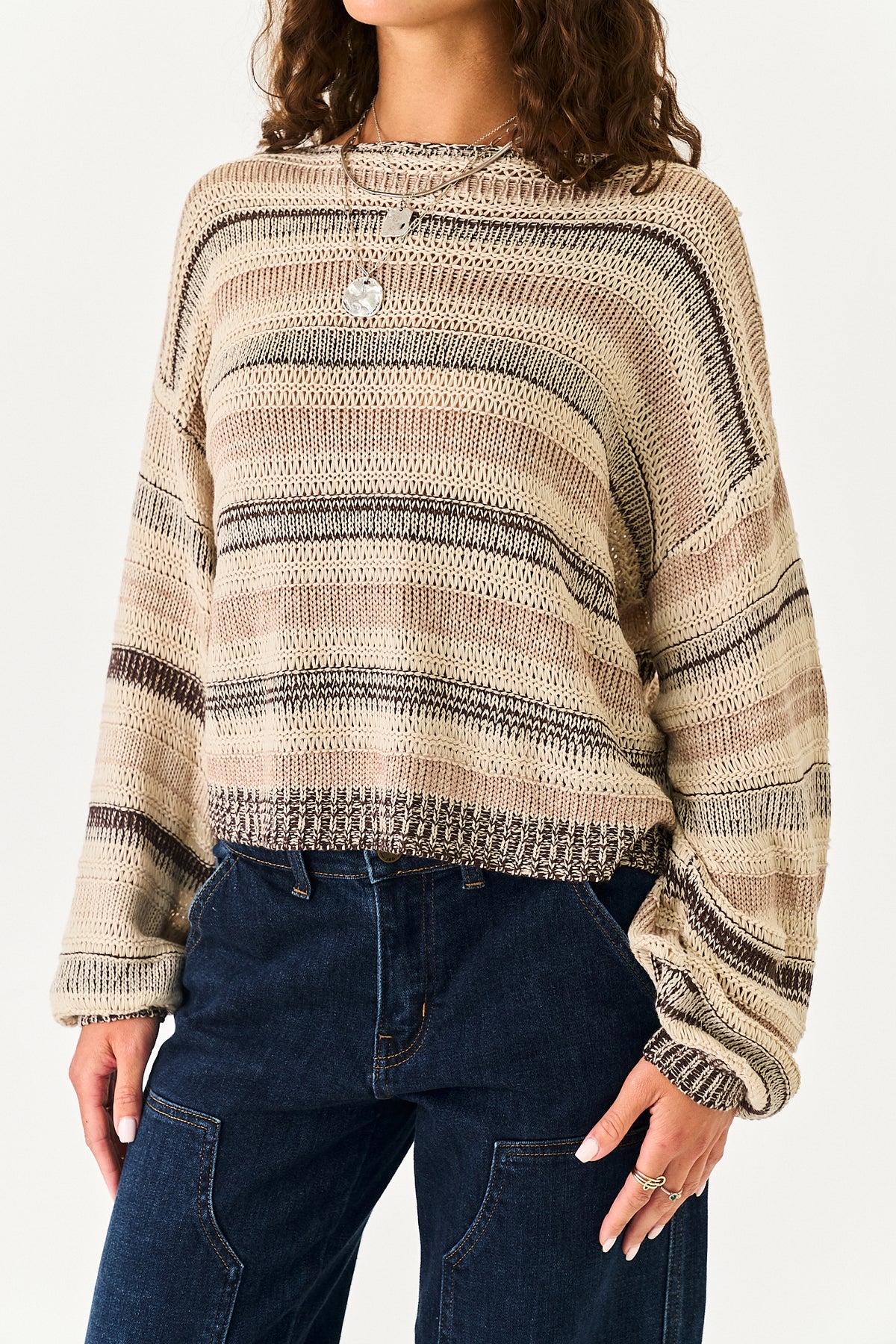 A woman wearing a beige and brown striped knit sweater with dark blue jeans, shown from the neck down against a plain white background.