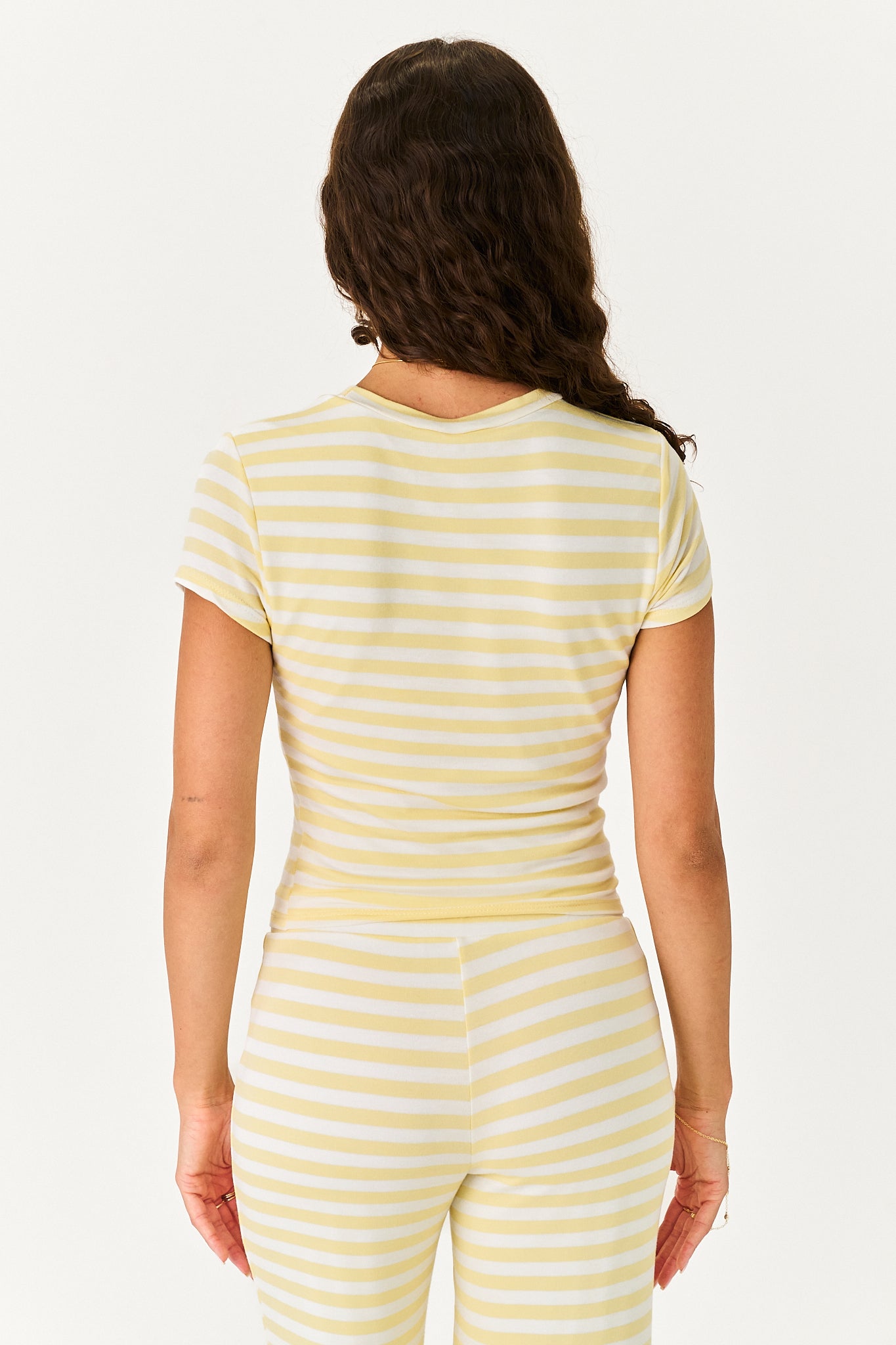 A woman viewed from behind wearing a pale yellow and white horizontally striped short-sleeve top and matching striped pants against a plain light background.
