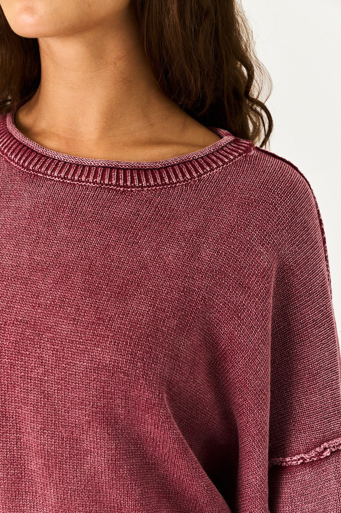 Close-up of a person wearing a ribbed crewneck sweater in a heathered dusty rose or mauve color, showing the knit texture and shoulder detail against a plain light background.