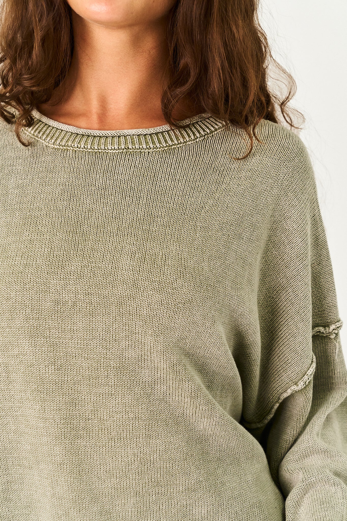 Close-up of a person wearing a ribbed knit sweater in a muted sage green color, showing the crew neckline and textured fabric.