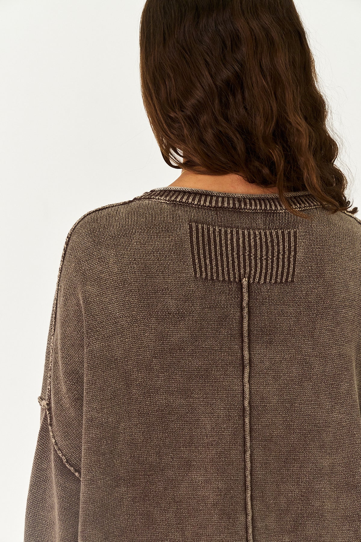 Back view of a person wearing a brown ribbed knit sweater against a plain white background.