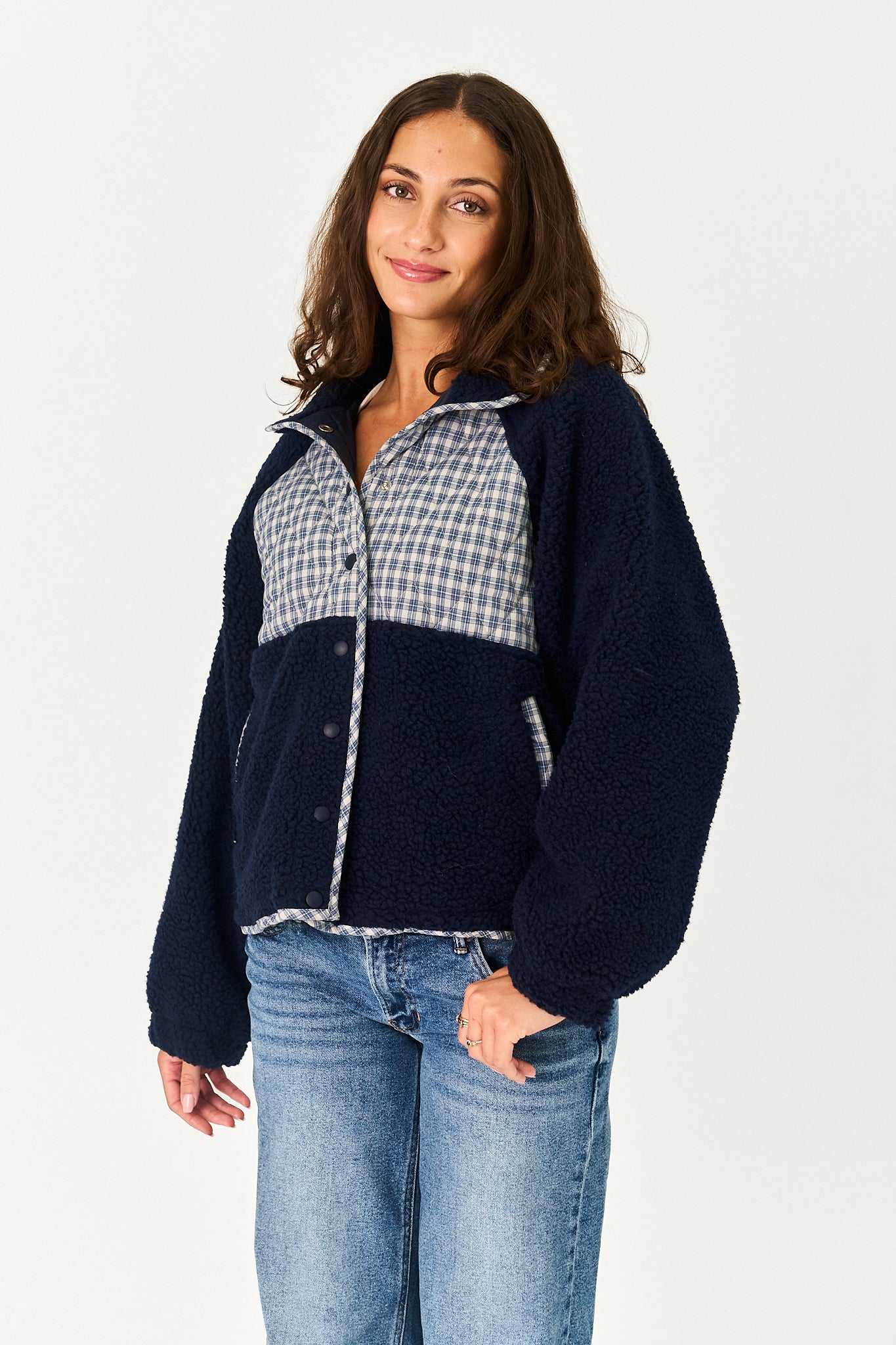 A woman modeling a navy blue fleece jacket with a light blue and white gingham patterned yoke and zipper trim, paired with blue jeans, against a plain white studio background.