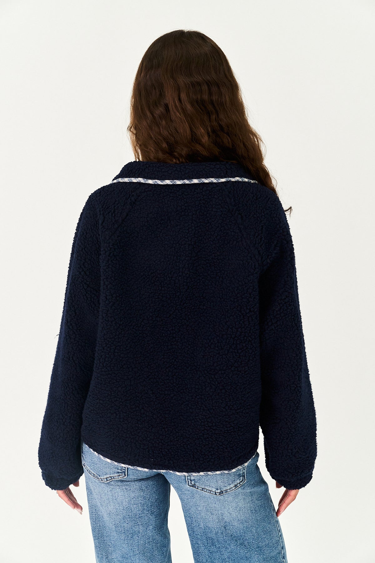 A woman viewed from the back wearing a dark navy blue sherpa fleece jacket with a white textured trim along the collar, paired with light blue jeans, against a plain white background.
