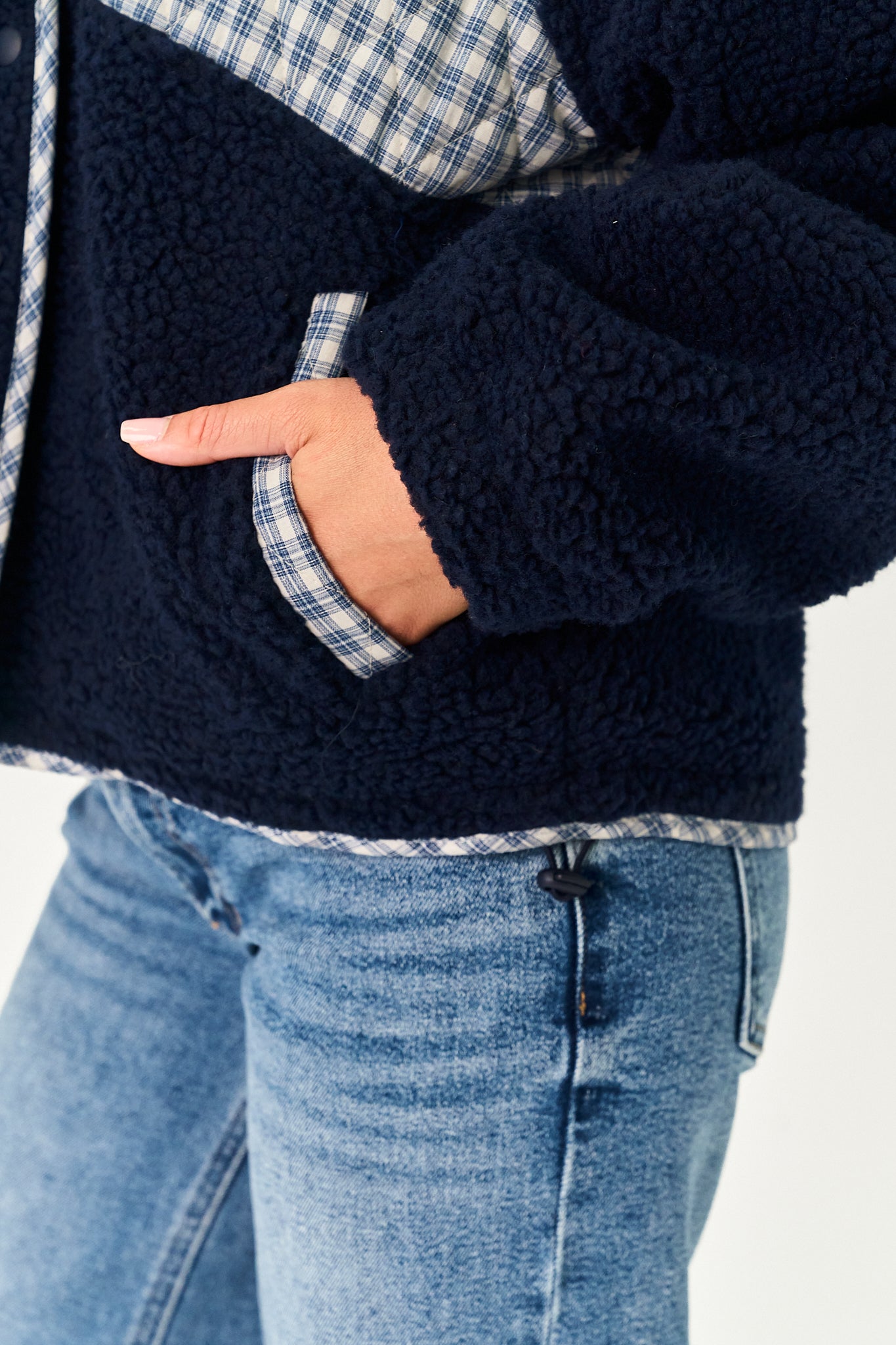 Close-up of a person wearing a navy fleece jacket with a blue and white plaid lining, paired with light blue jeans.