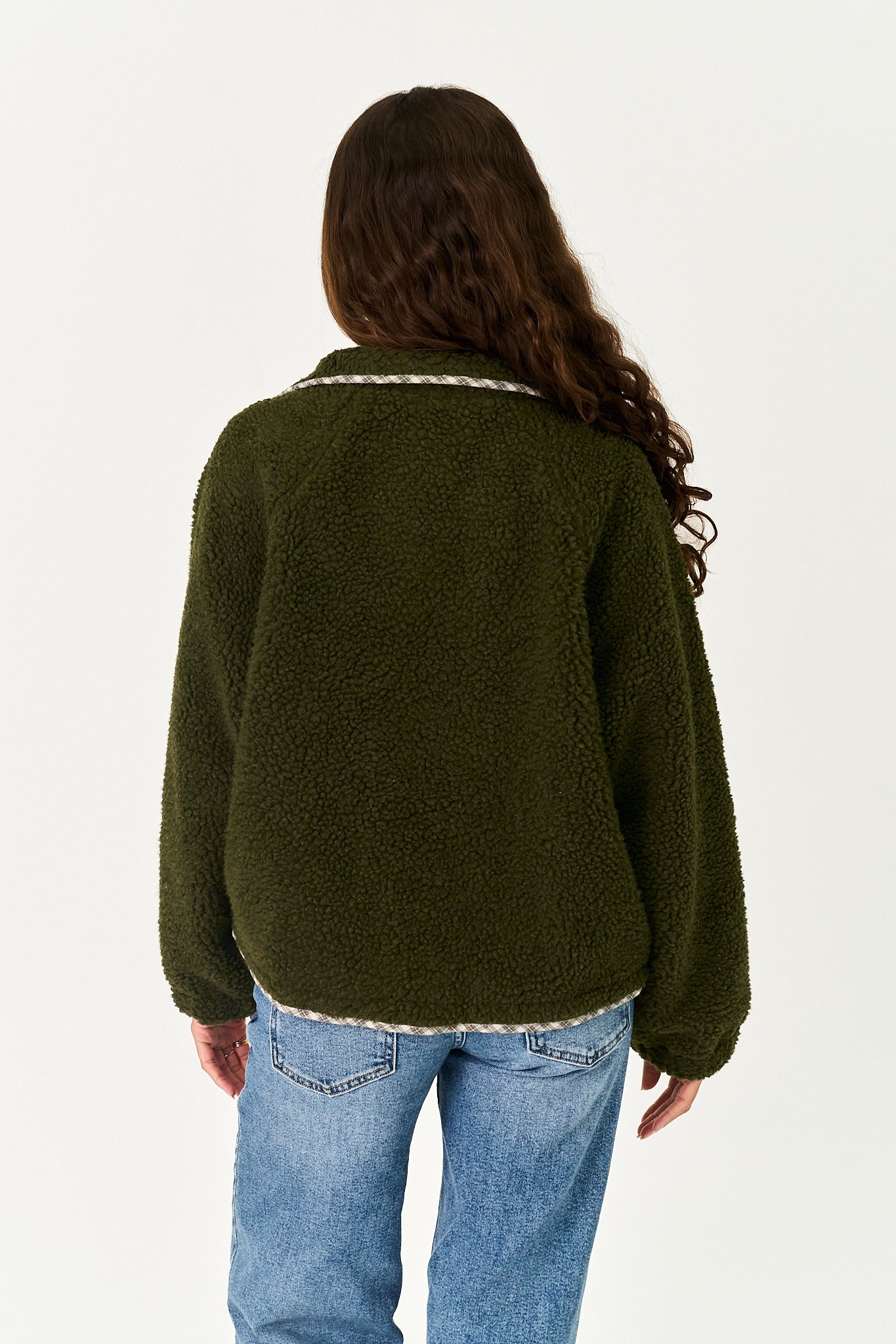 A woman viewed from the back wearing an olive green sherpa fleece jacket with a white textured trim along the collar and hem, paired with blue jeans, against a plain white background.