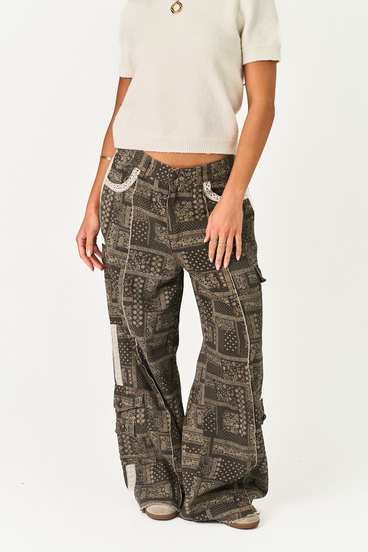 A model wearing a pair of wide-leg cargo pants with a dark brown and beige geometric patchwork print, styled with a cream short-sleeve crop top against a white studio background.