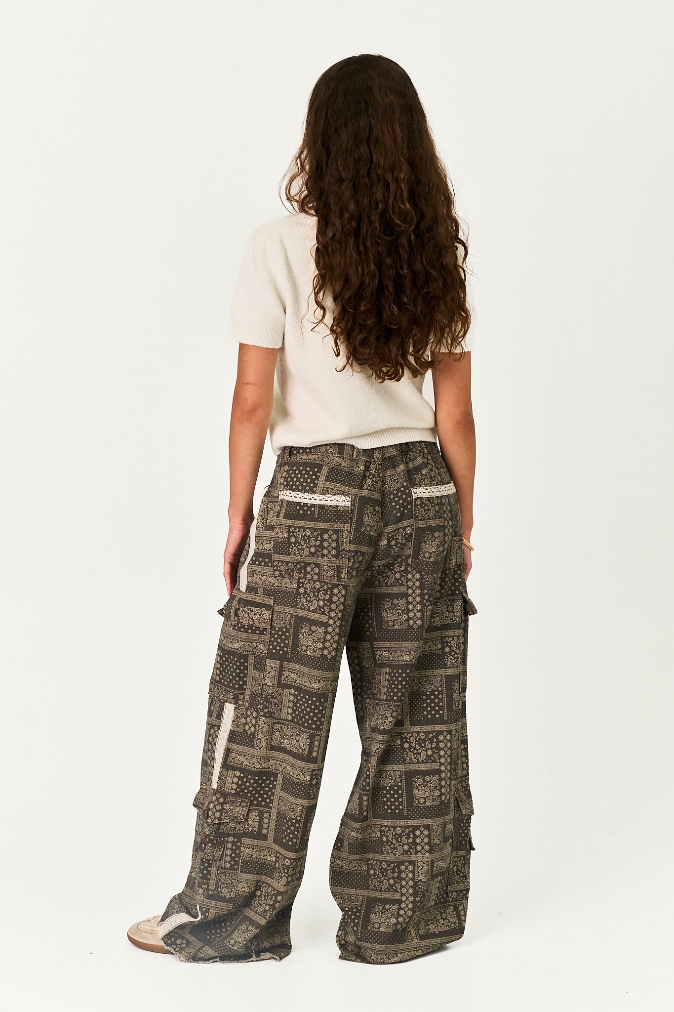A model shown from the back wearing wide-leg cargo pants with a brown and beige geometric pattern, paired with a cream t-shirt, against a plain white studio background.