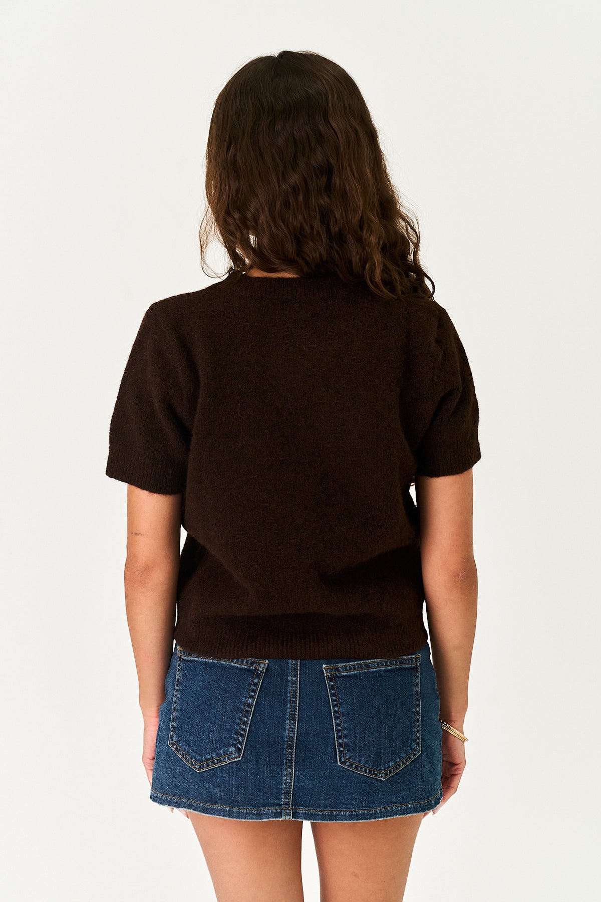 A model shown from the back wearing a dark brown short-sleeve knit top and a blue denim mini skirt against a plain white background.