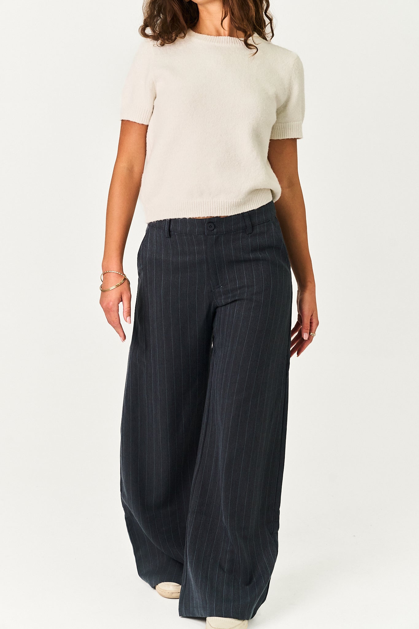 A model is shown from the back wearing a cream short-sleeve knit top and dark navy wide-leg pinstripe trousers against a plain white studio background.