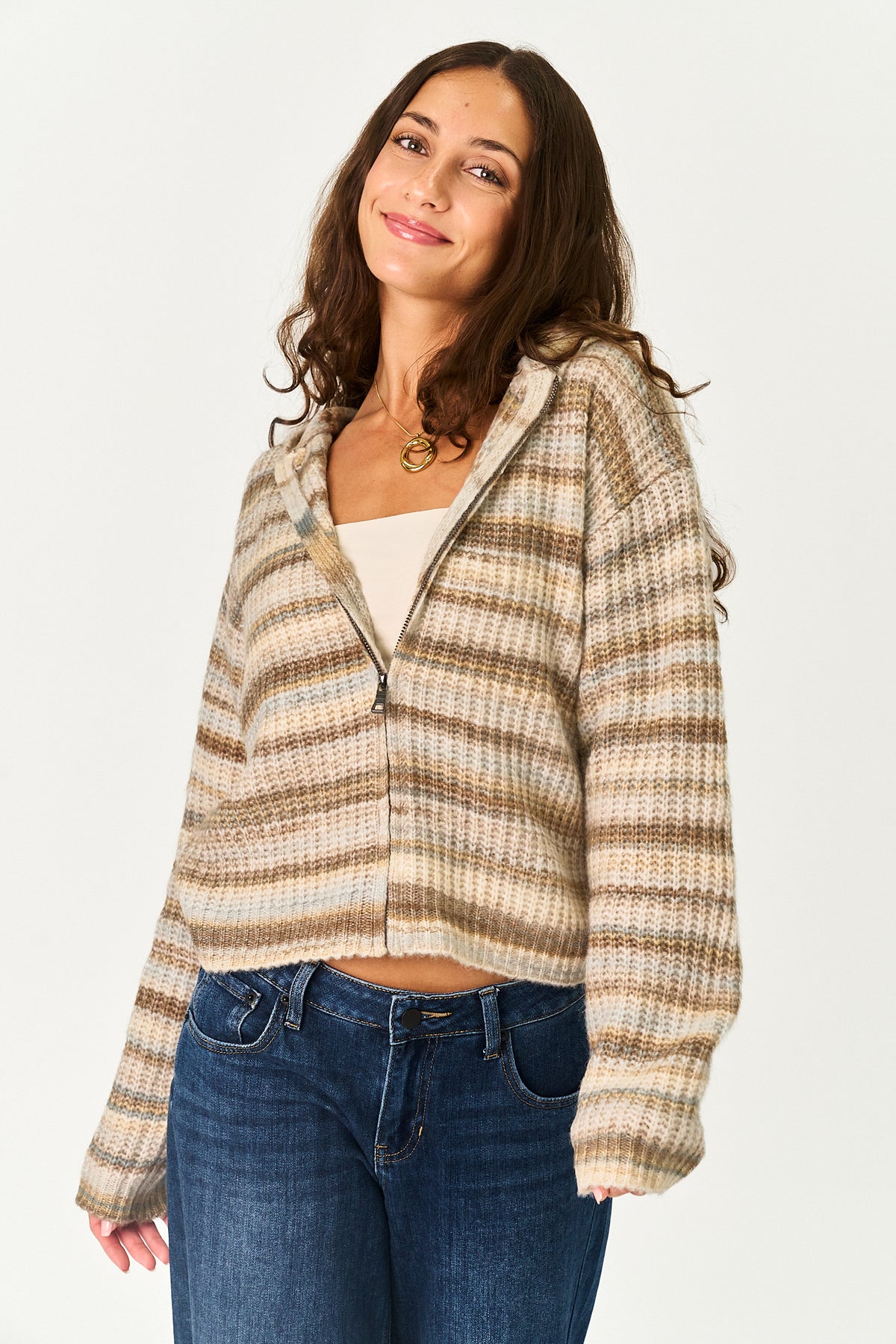 A woman modeling a cropped, zip-up hooded sweater with a beige and brown plaid pattern, worn over a white tank top and blue jeans against a plain white background.