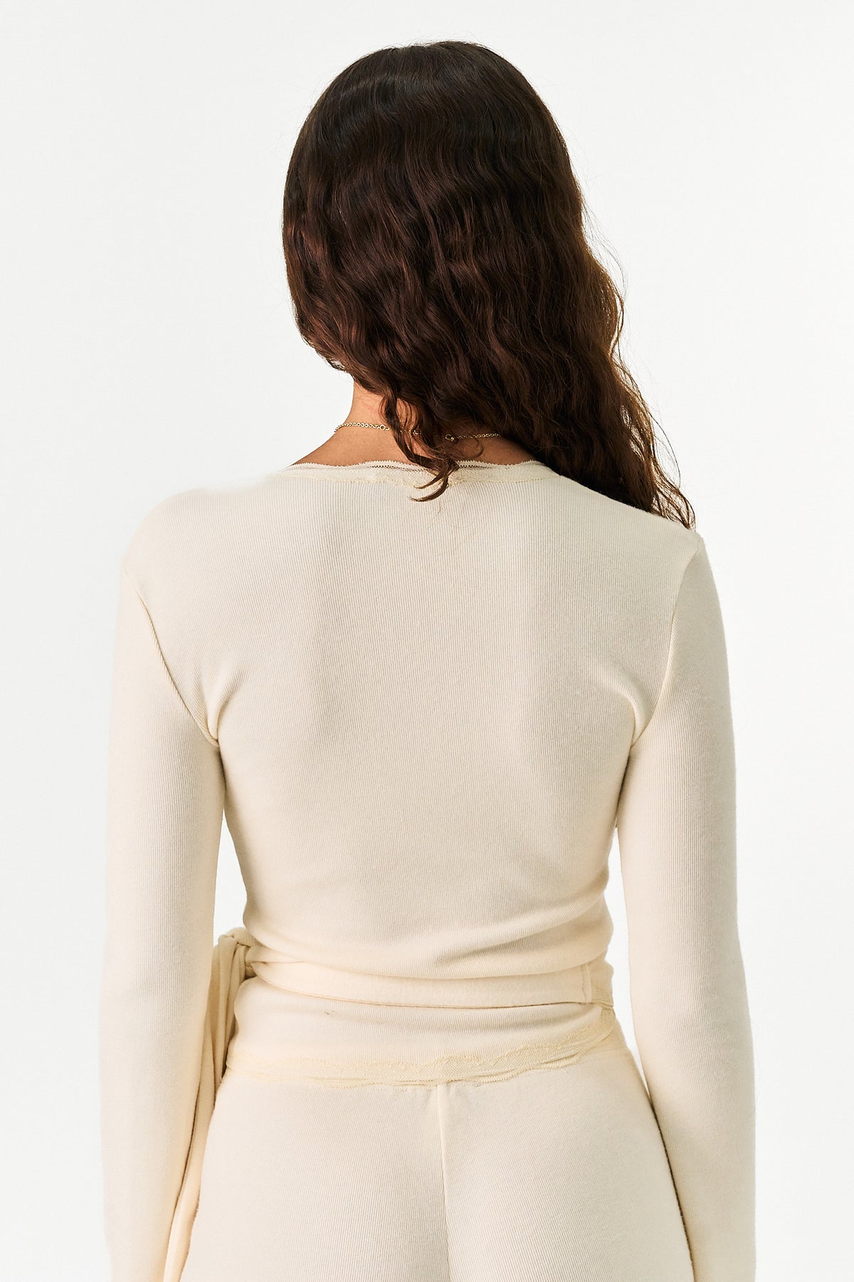 A woman shown from the back wearing a cream-colored long-sleeve knit top and matching bottoms against a plain white studio background.