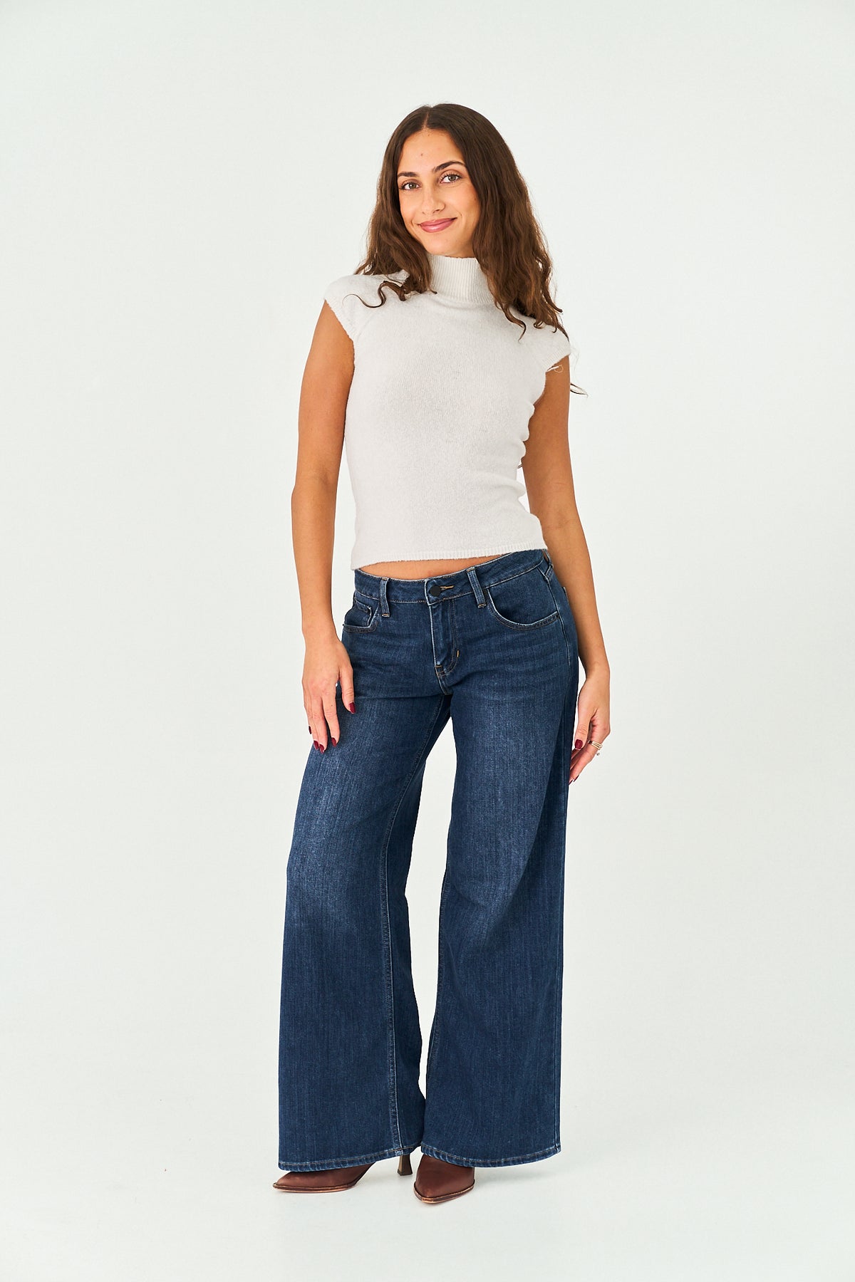A woman modeling a white ribbed mock-neck top and dark blue wide-leg denim jeans against a plain white studio background.