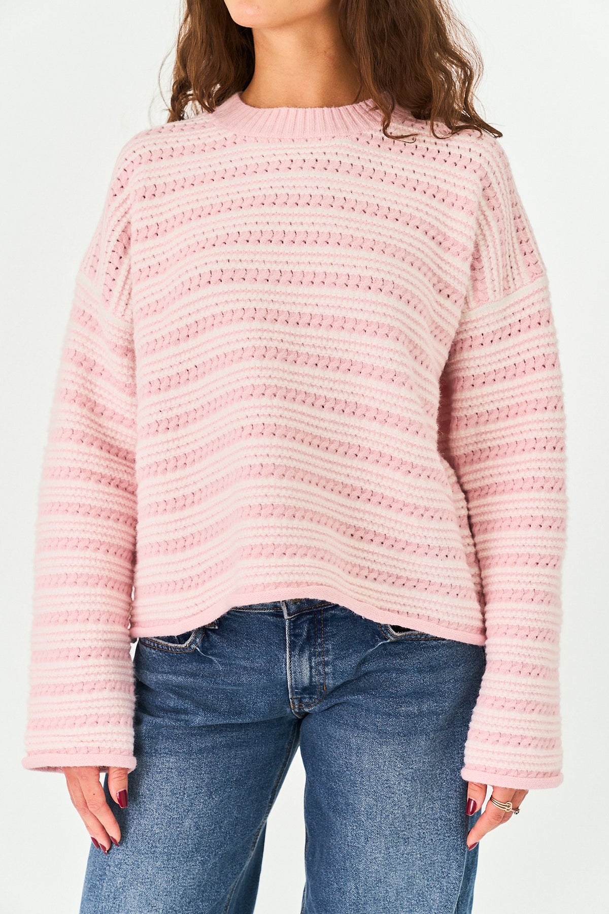 A woman wearing a light pink and white horizontally striped knit sweater with blue jeans, shown from the neck down against a plain white background.
