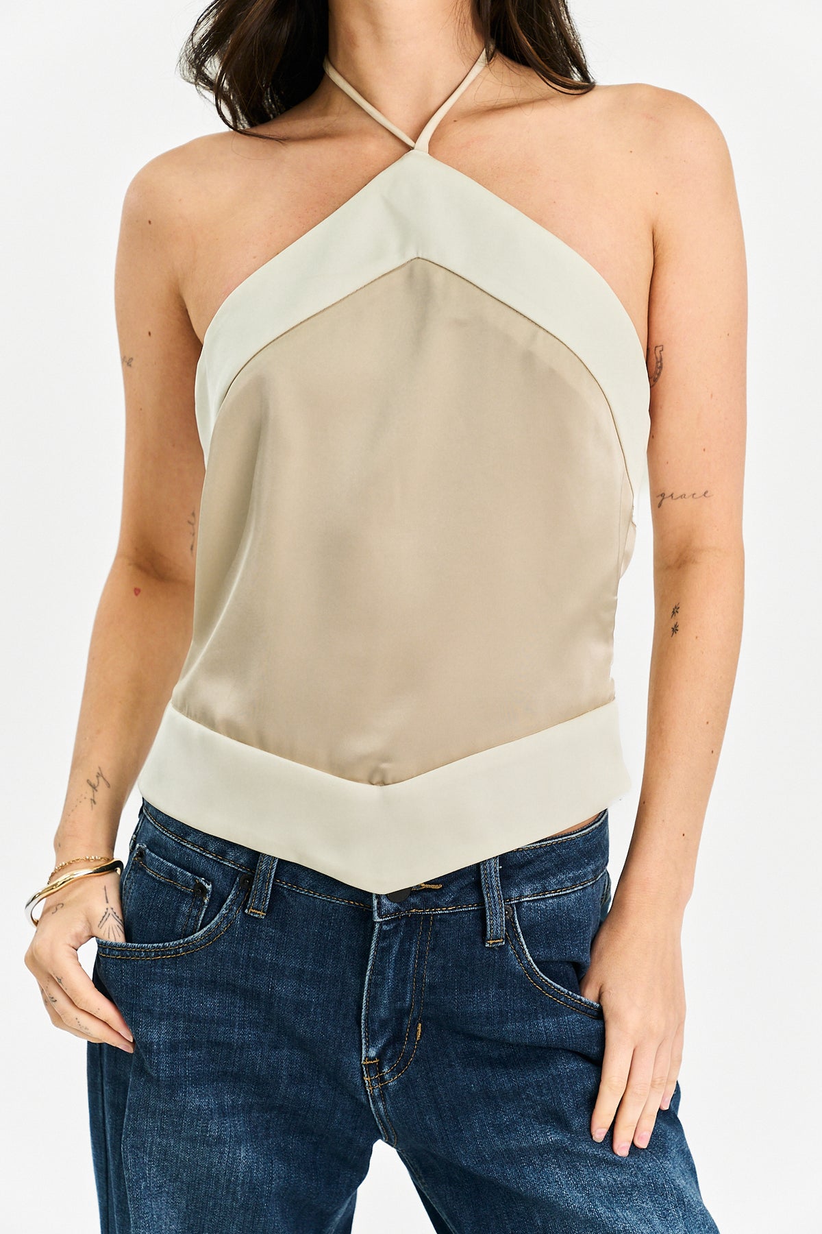 A woman wearing a beige and off-white halter top with a geometric color-blocked design, paired with blue jeans, against a plain white background.