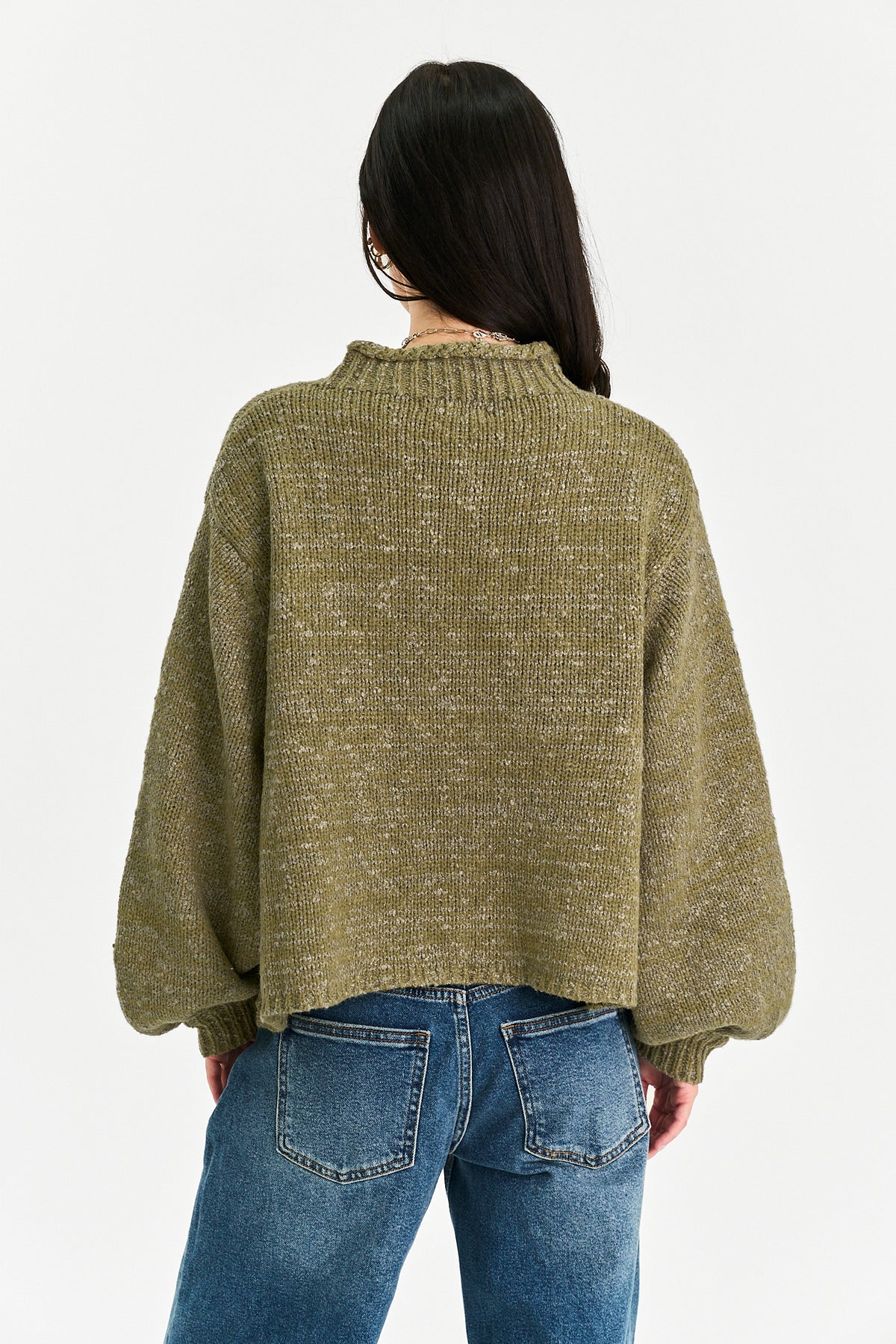 A woman viewed from the back wearing an oversized olive green knit sweater and blue jeans against a plain light background.