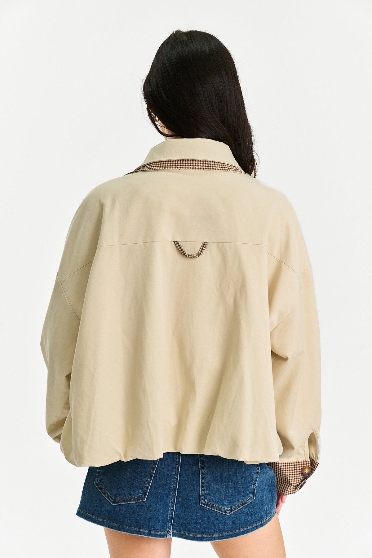 A woman shown from the back wearing a beige oversized button-up shirt with a brown and beige checkered collar and cuffs, paired with blue denim shorts, against a plain white background.