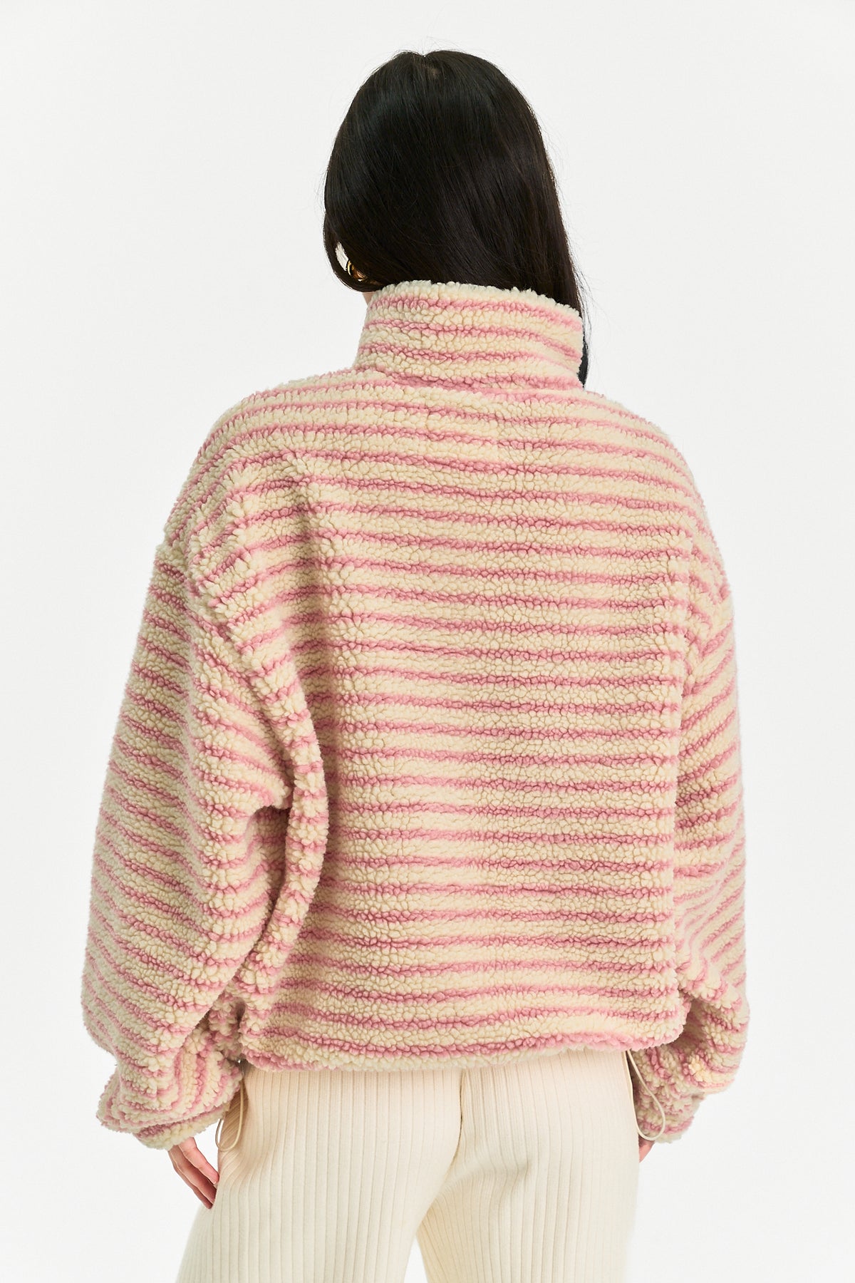 A person shown from the back wearing a fuzzy striped knit top in light pink and cream, paired with cream ribbed pants, against a plain light background.