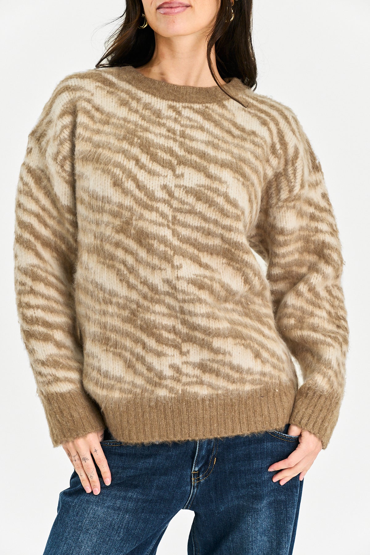 A woman wearing a beige and brown zebra-patterned knit sweater with blue jeans, shown from the nose down against a plain light background.