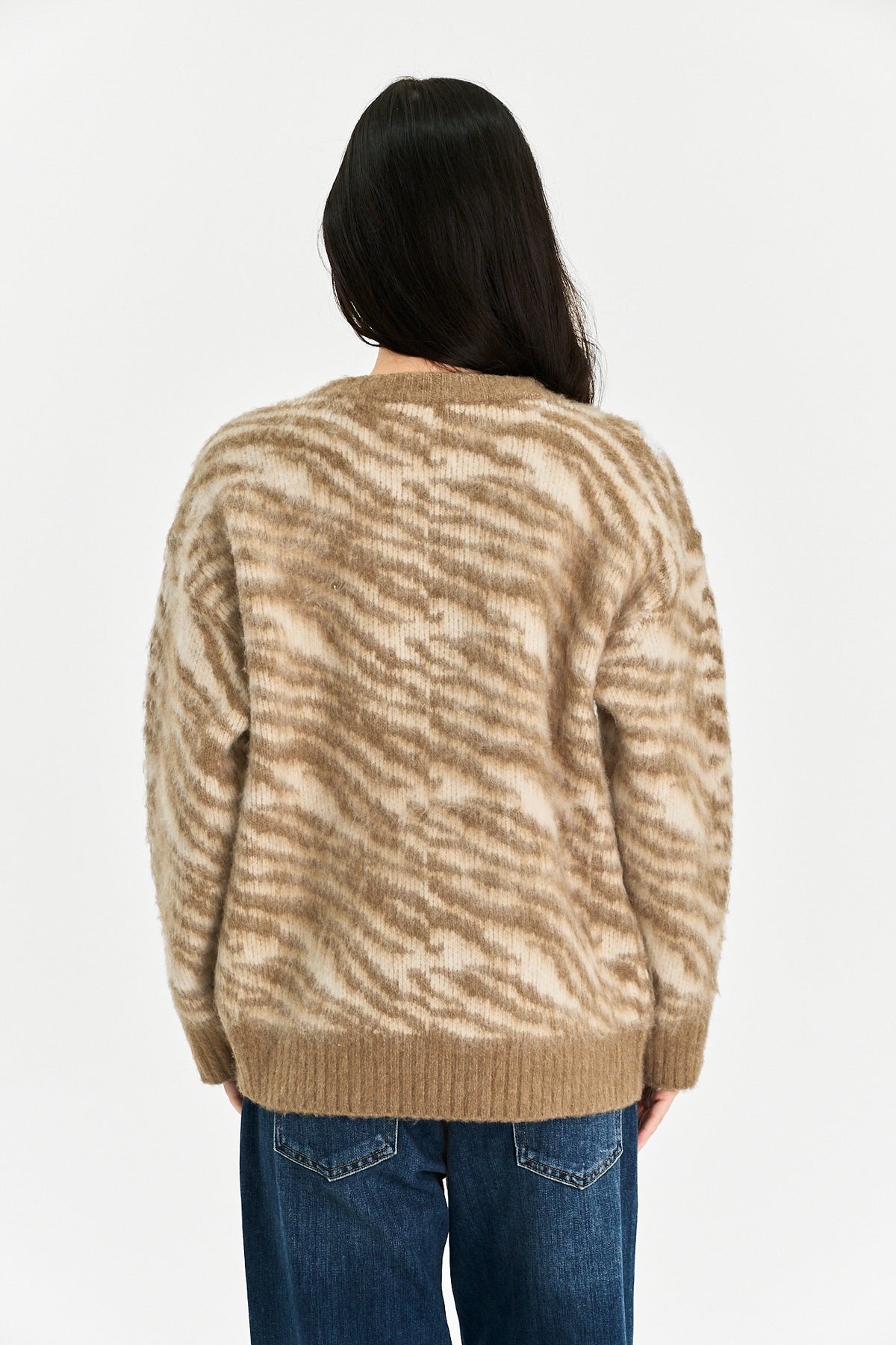 A person viewed from the back wearing a beige and cream zebra-patterned knit sweater with blue jeans, against a plain white background.