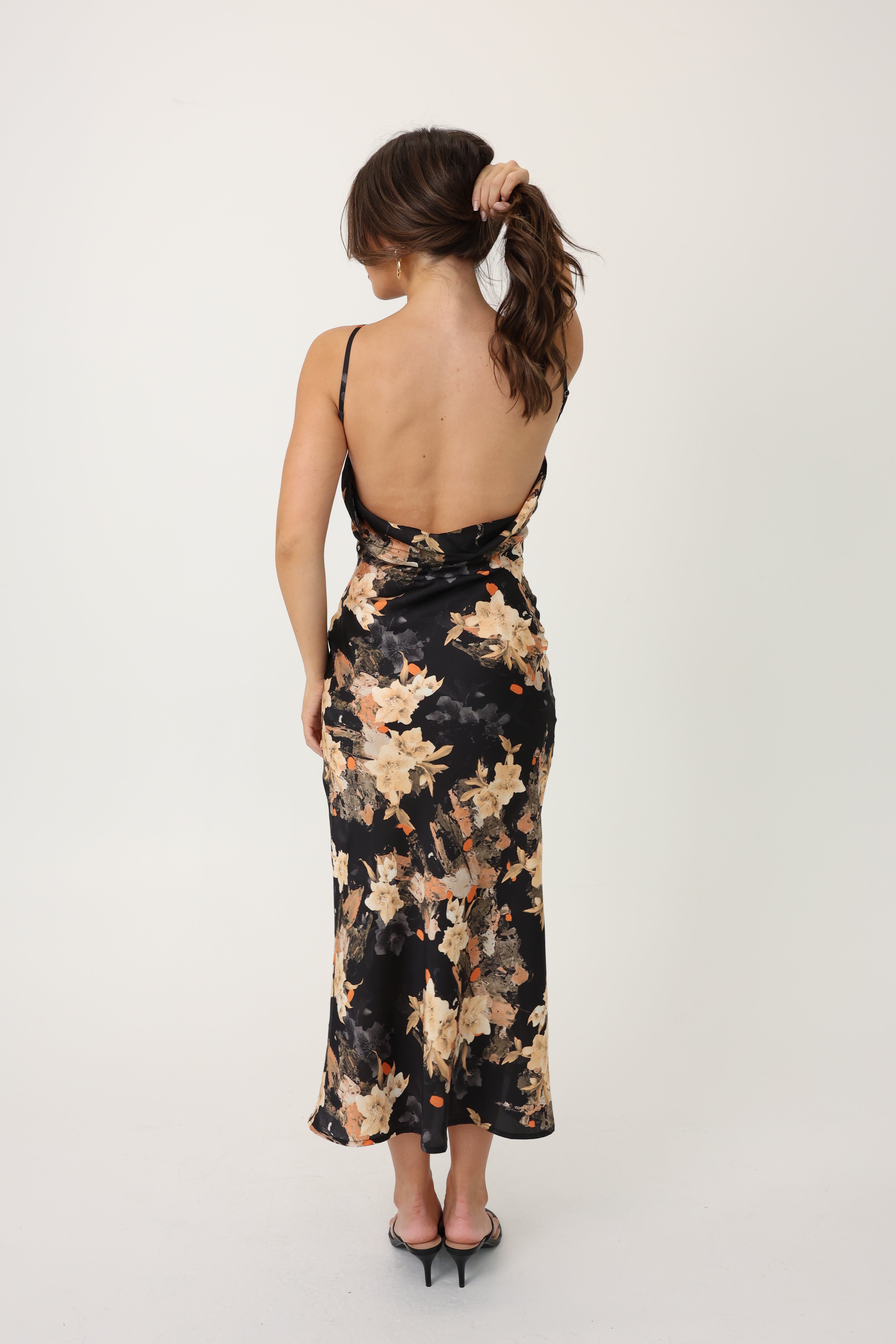 Woman wearing a black floral maxi dress with a deep open back with a white background