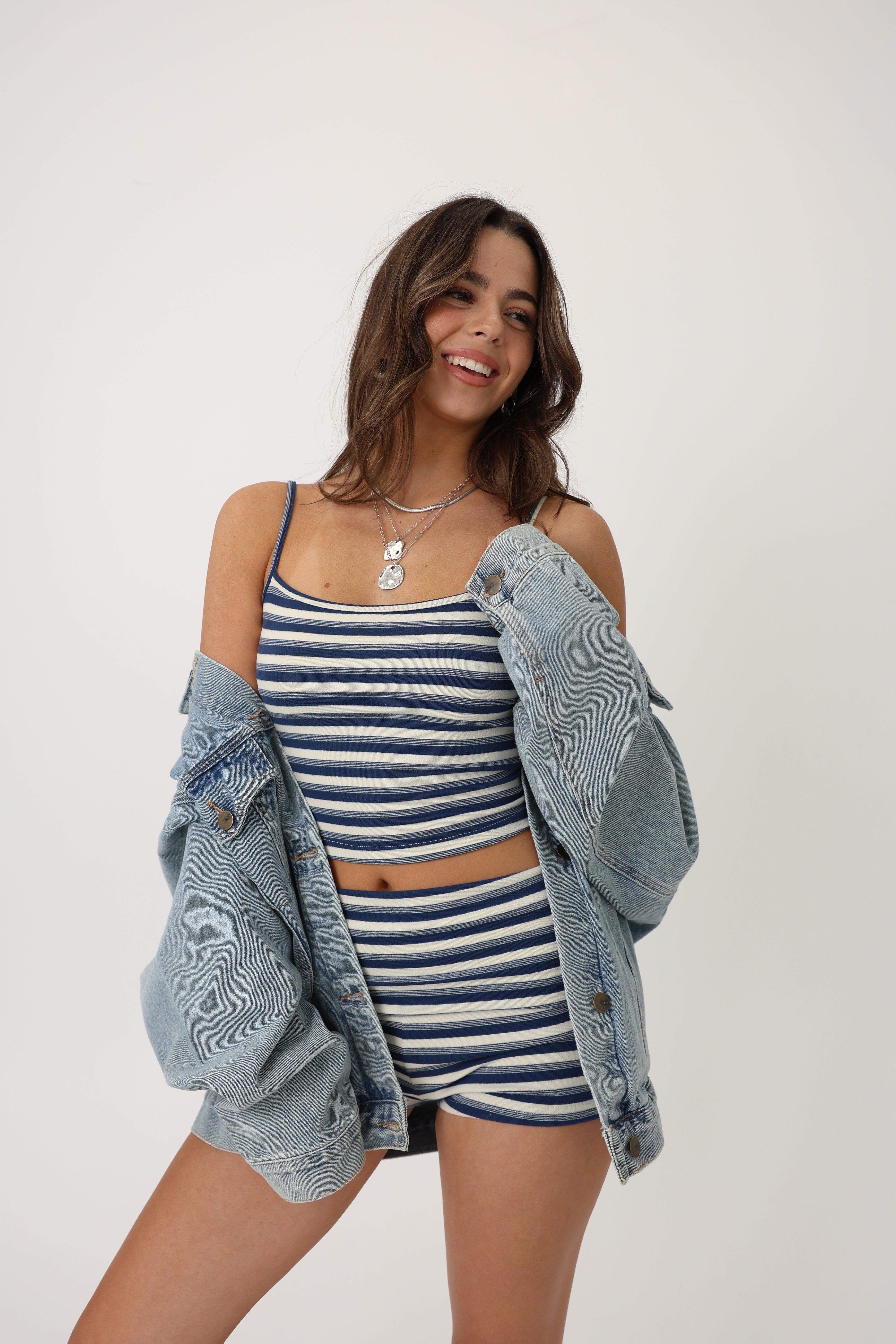 Person wearing a blue and white striped tank top and shorts set with denim jacket