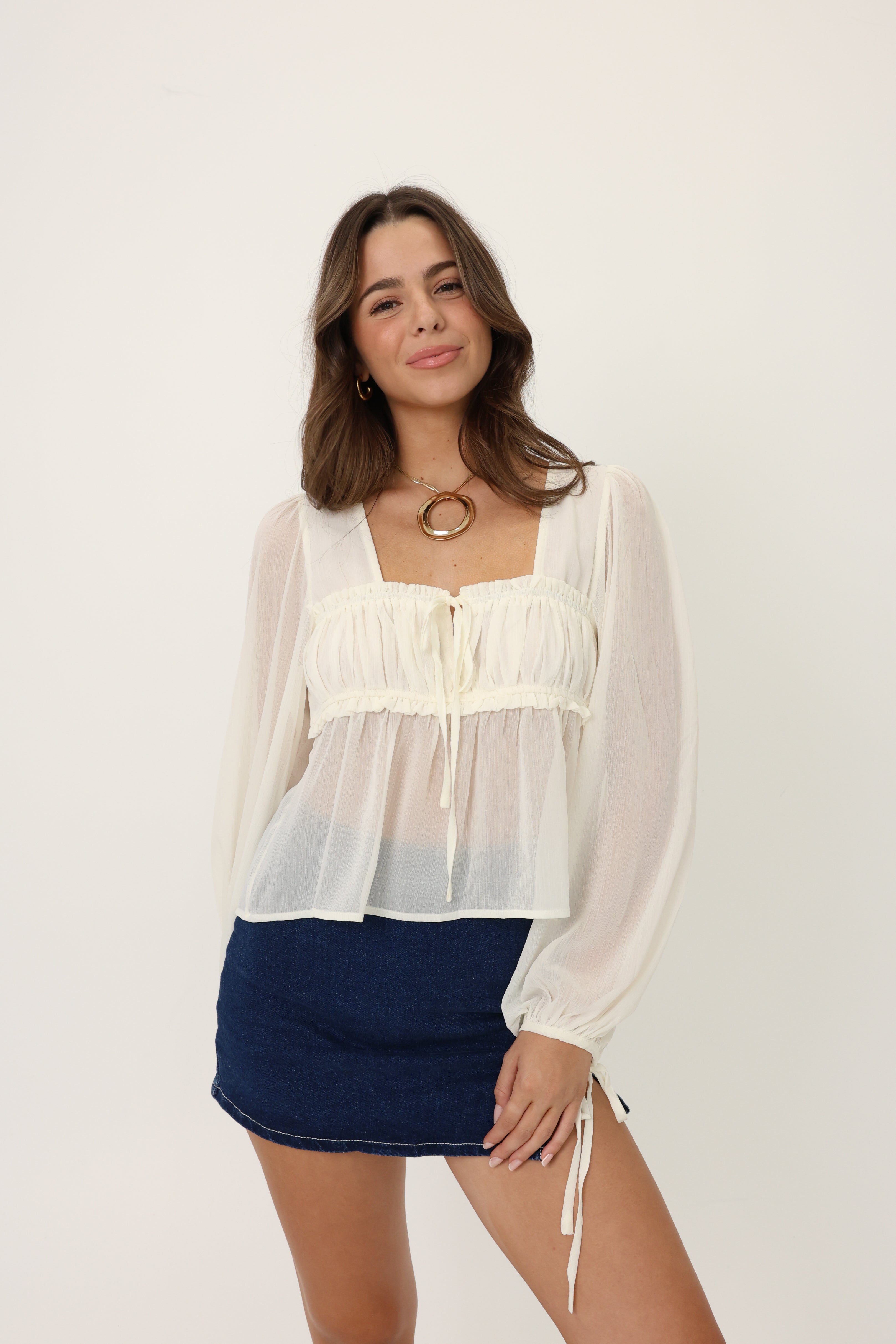 Woman wearing a white blouse with sheer sleeves and a navy skirt on a white background