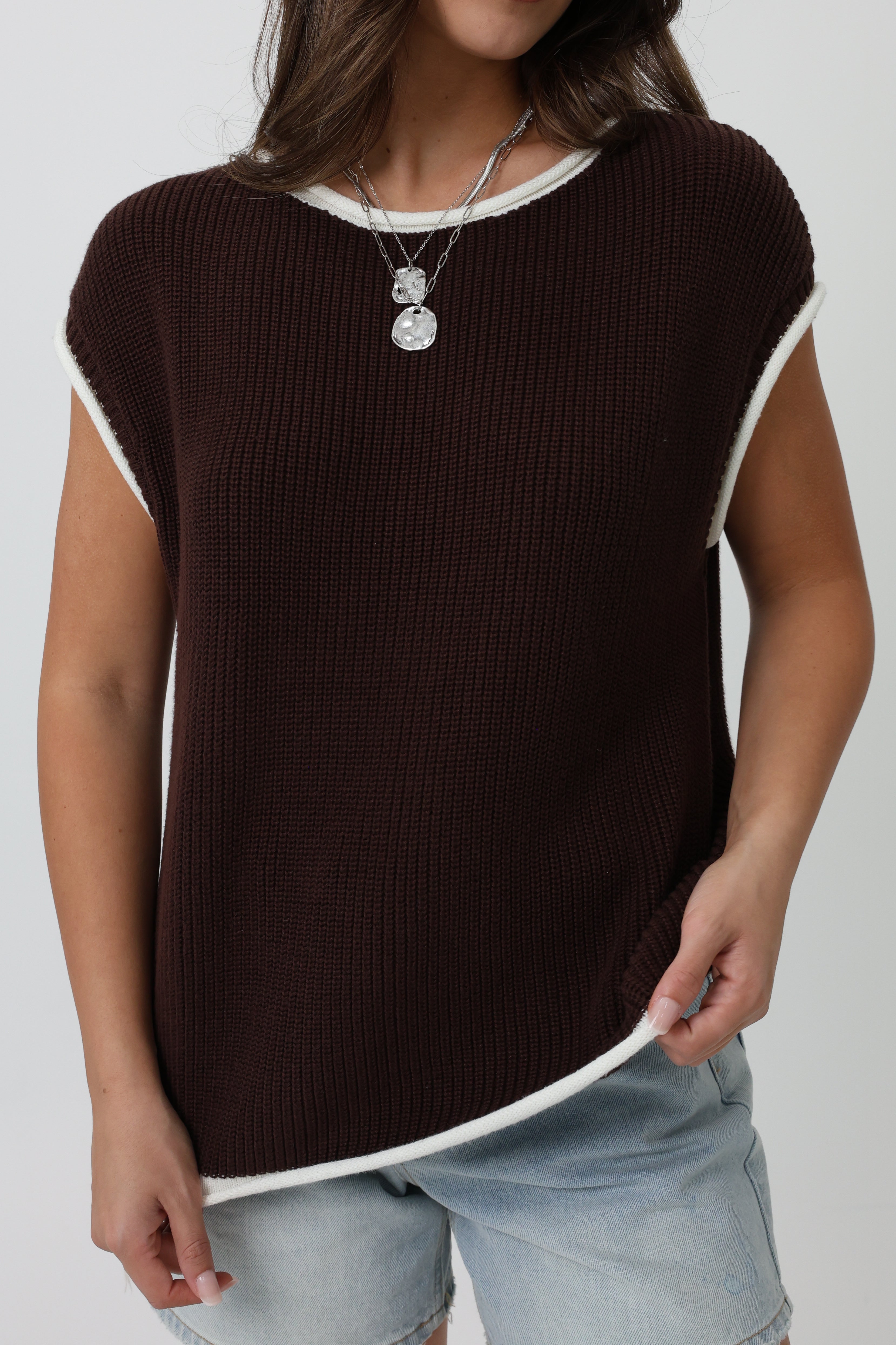 Woman wearing a brown ribbed sweater with white trim on a plain background