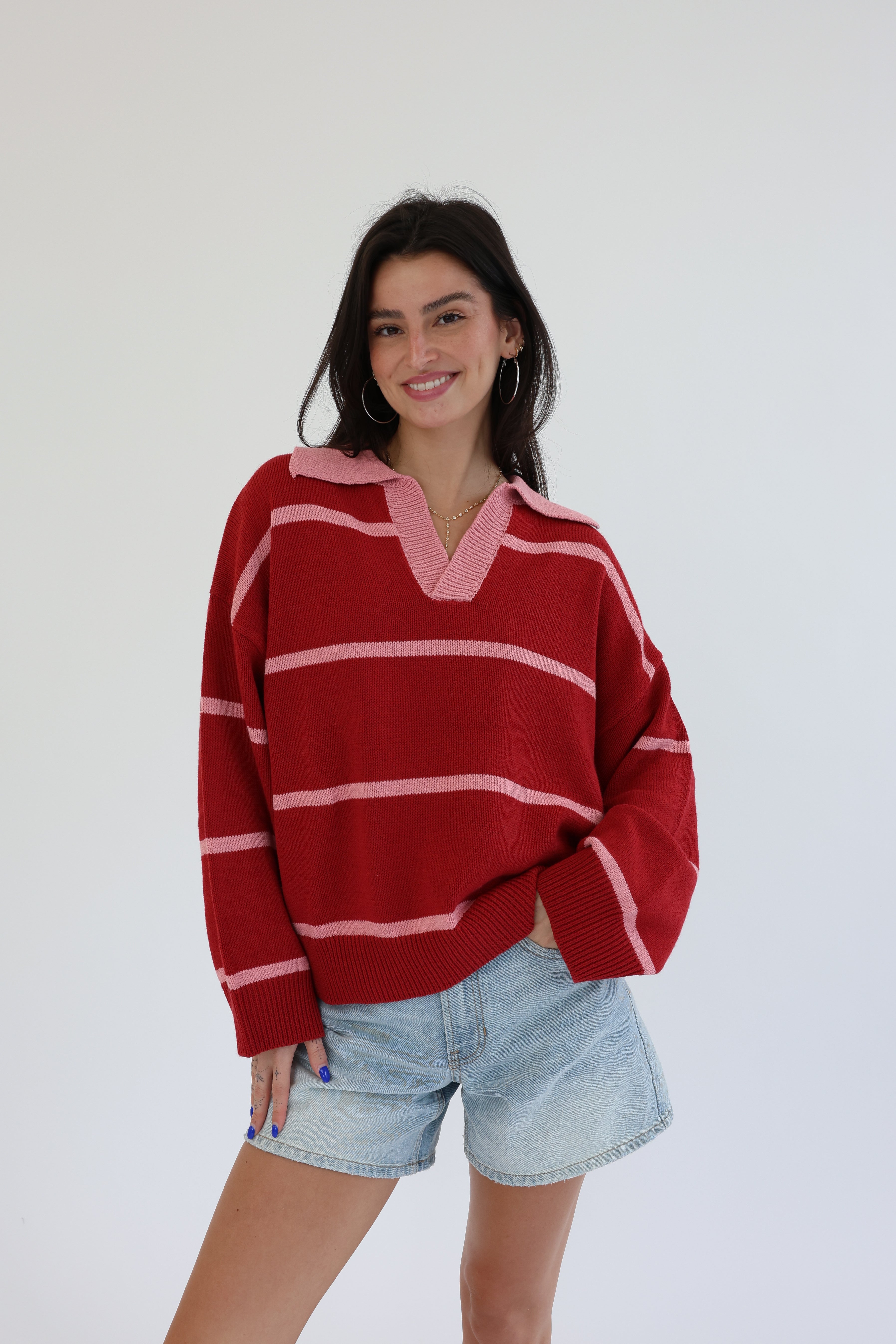 Woman wearing a red and pink striped sweater with denim shorts on a white background