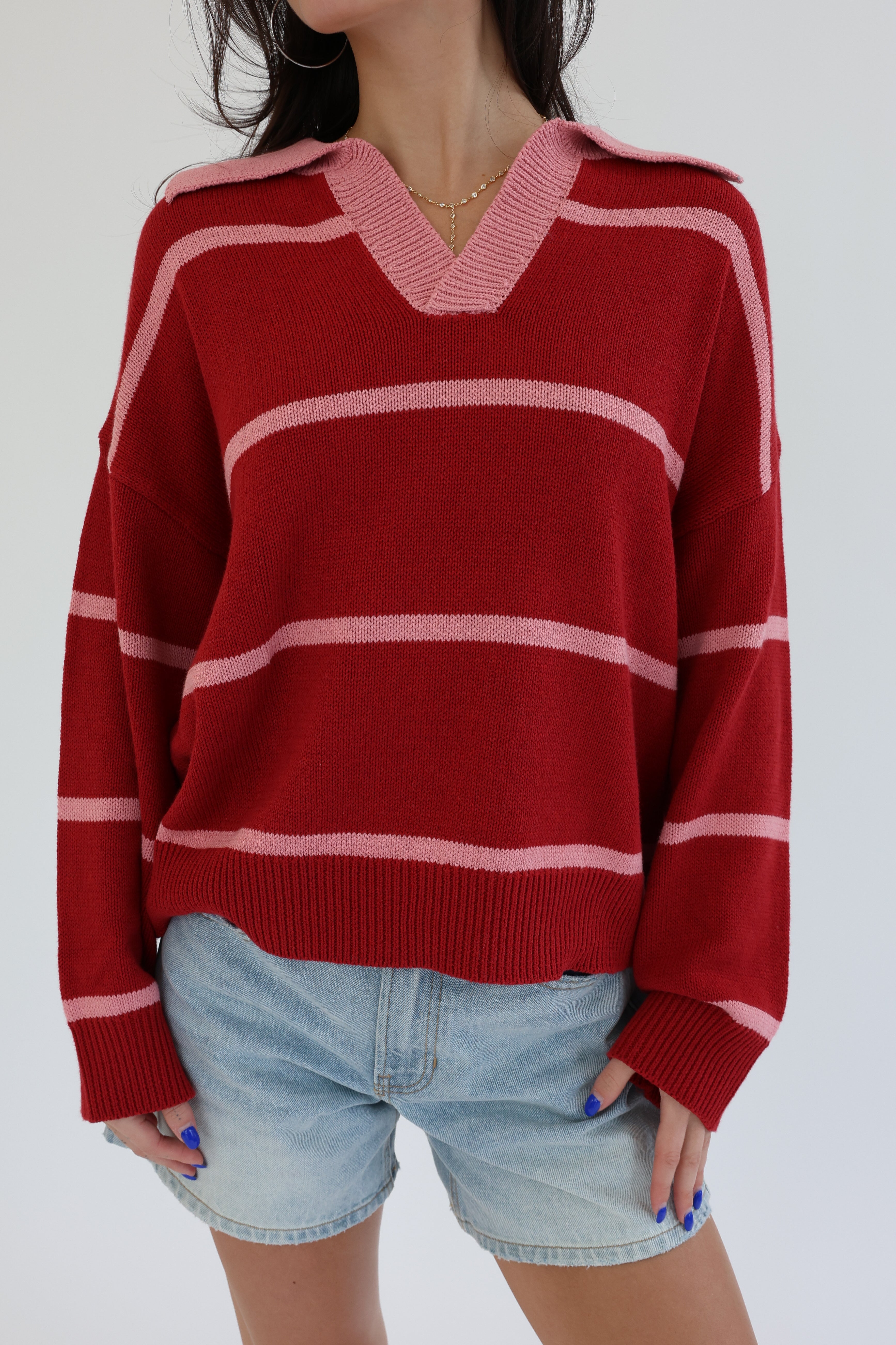 Person wearing a red and pink striped sweater with denim shorts on a white background