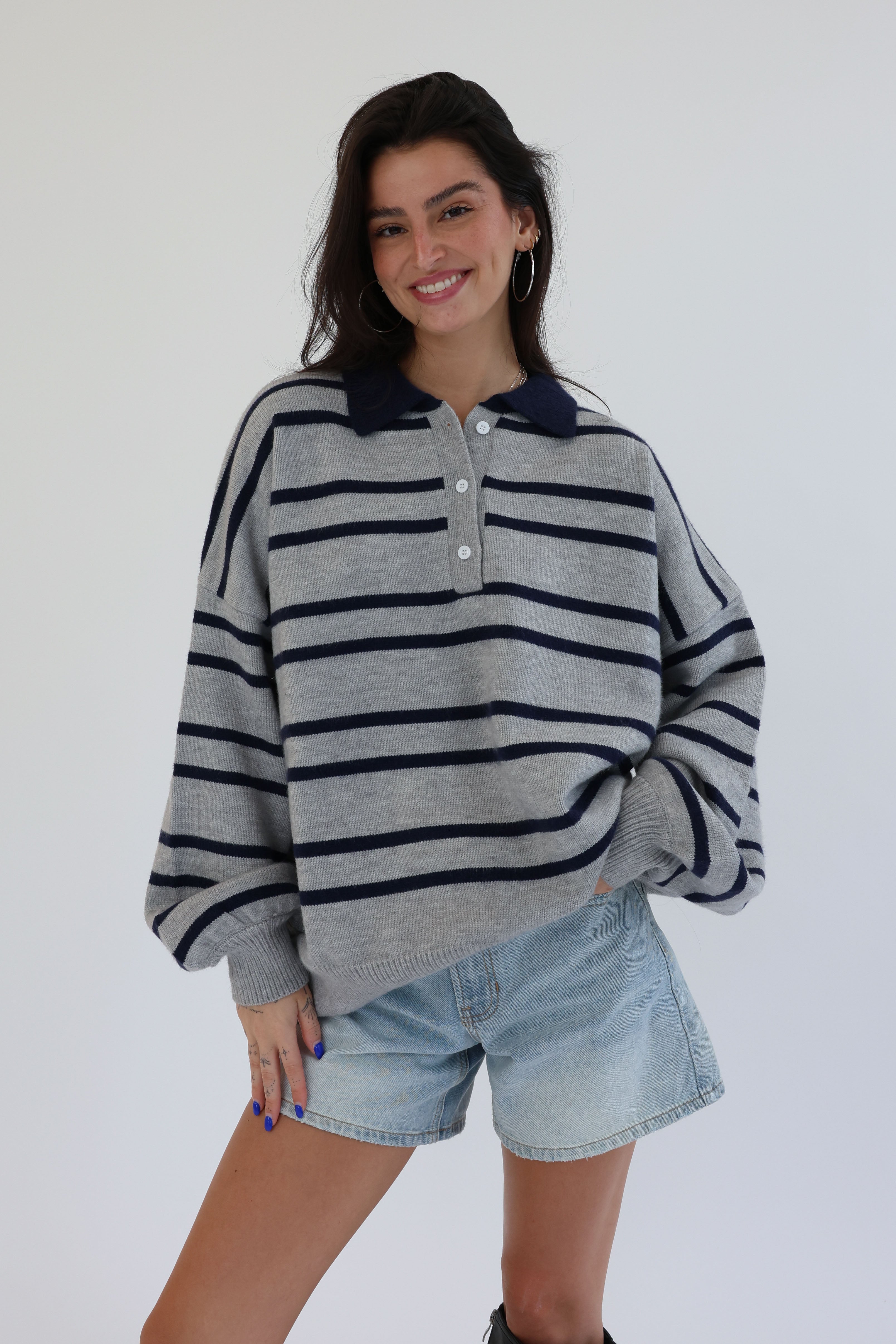 Woman wearing a gray sweater with navy stripes and denim shorts on a white background